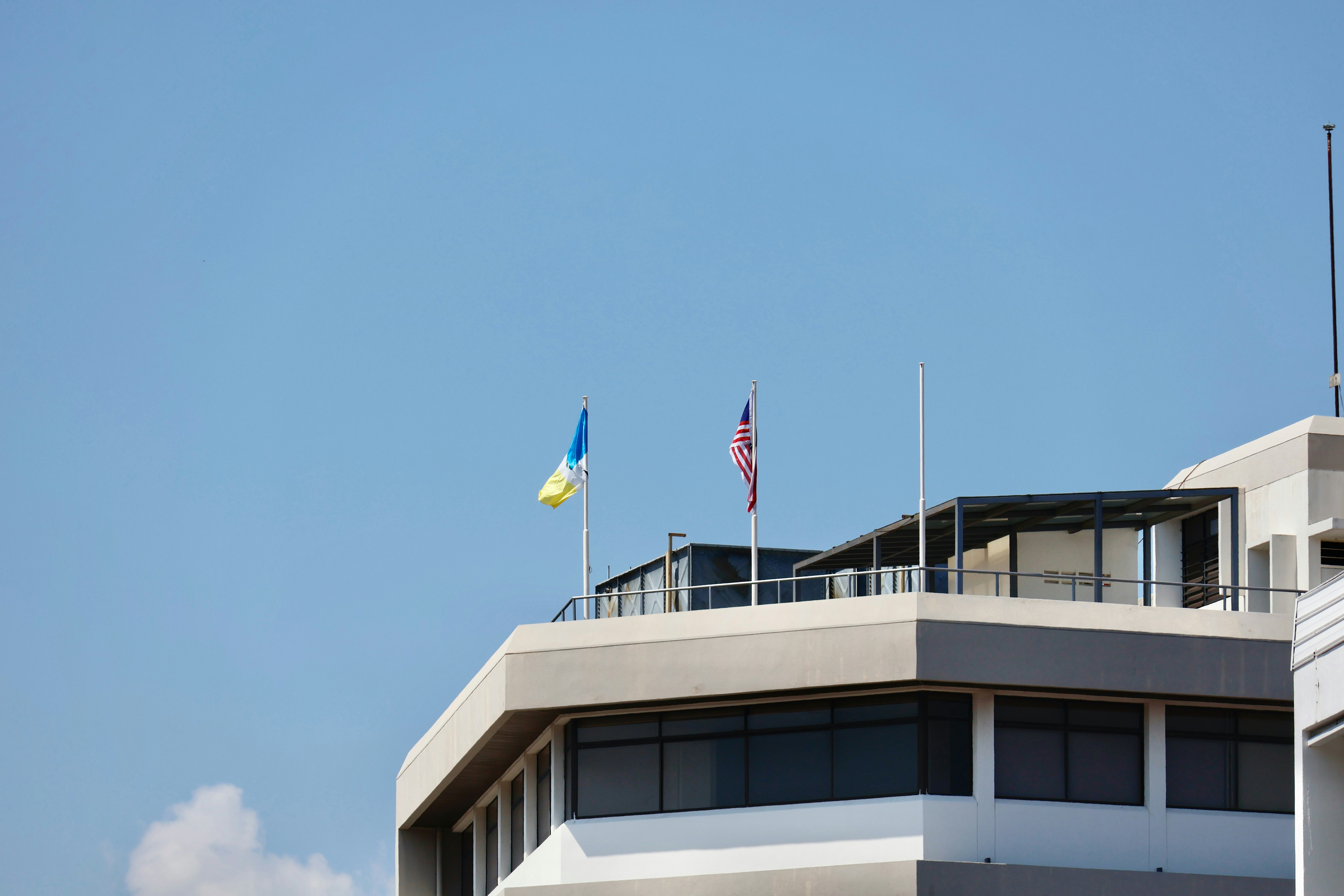 Two flags fly on a modern building rooftop.