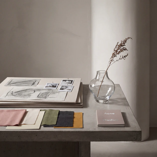 Fabric swatches, design sketches, and a glass vase on a studio table, representing an interior designer's planning process