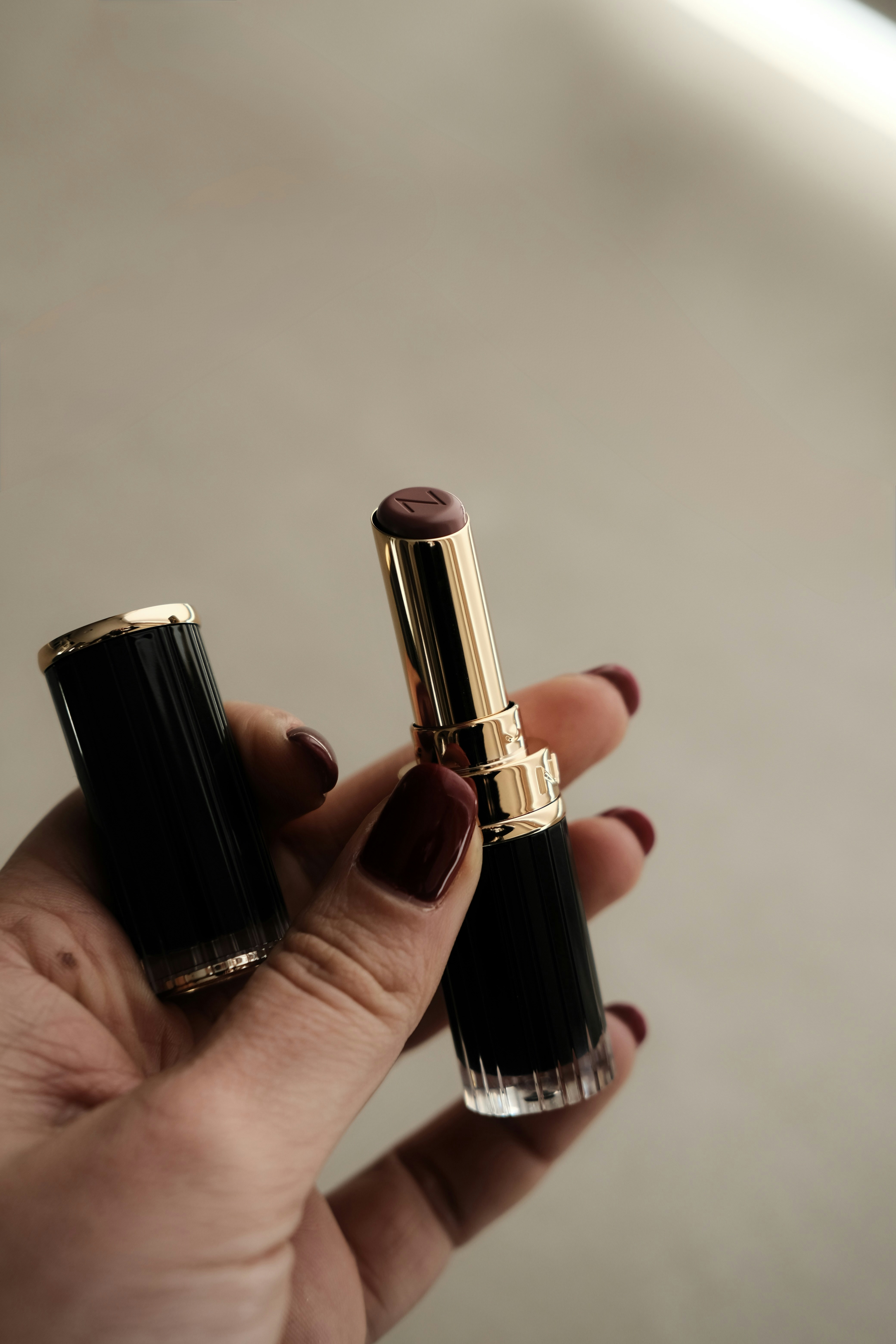 Hand hält offenen dunklen Lippenstift mit goldenen Akzenten