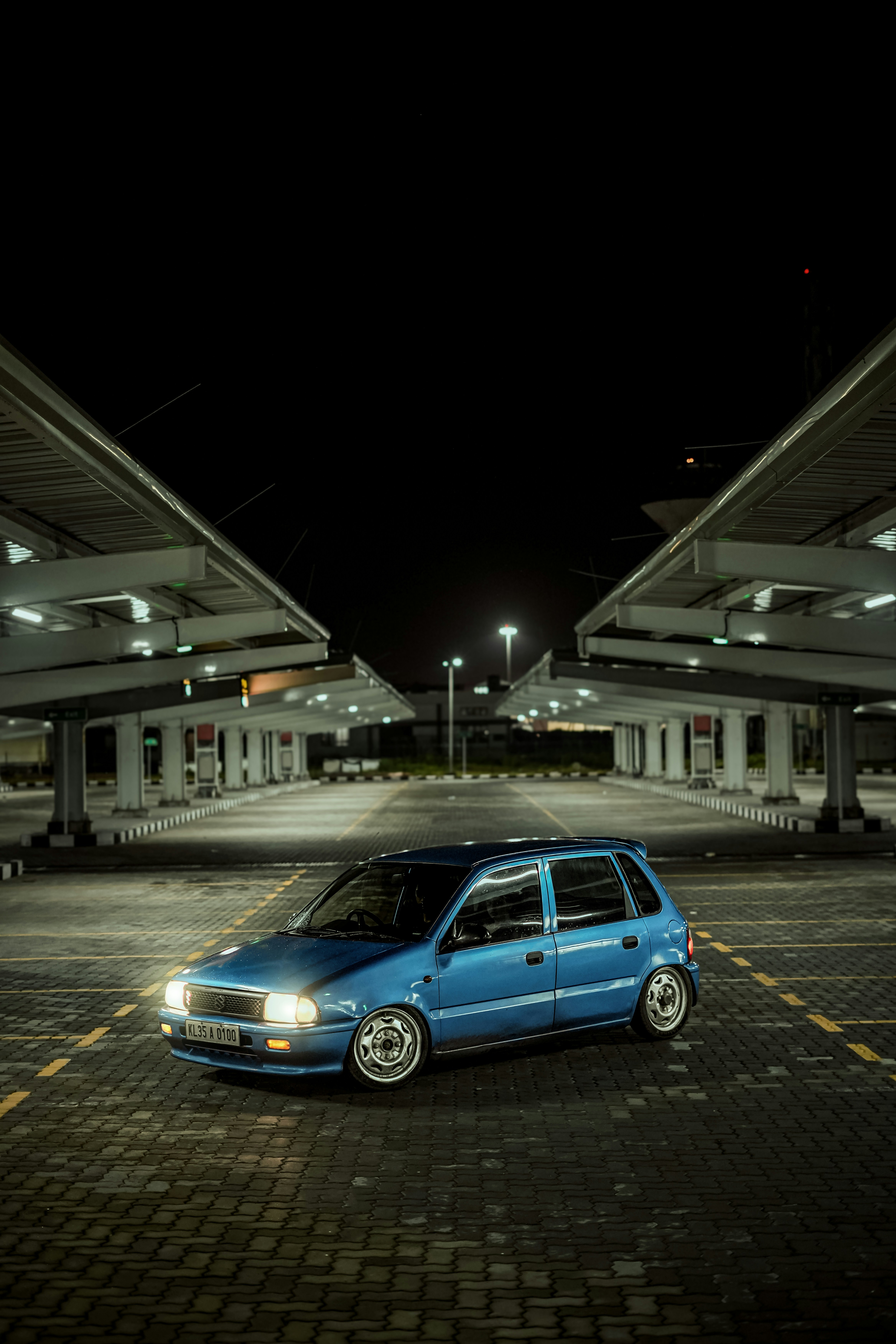 A blue car parked under a modern structure at night.