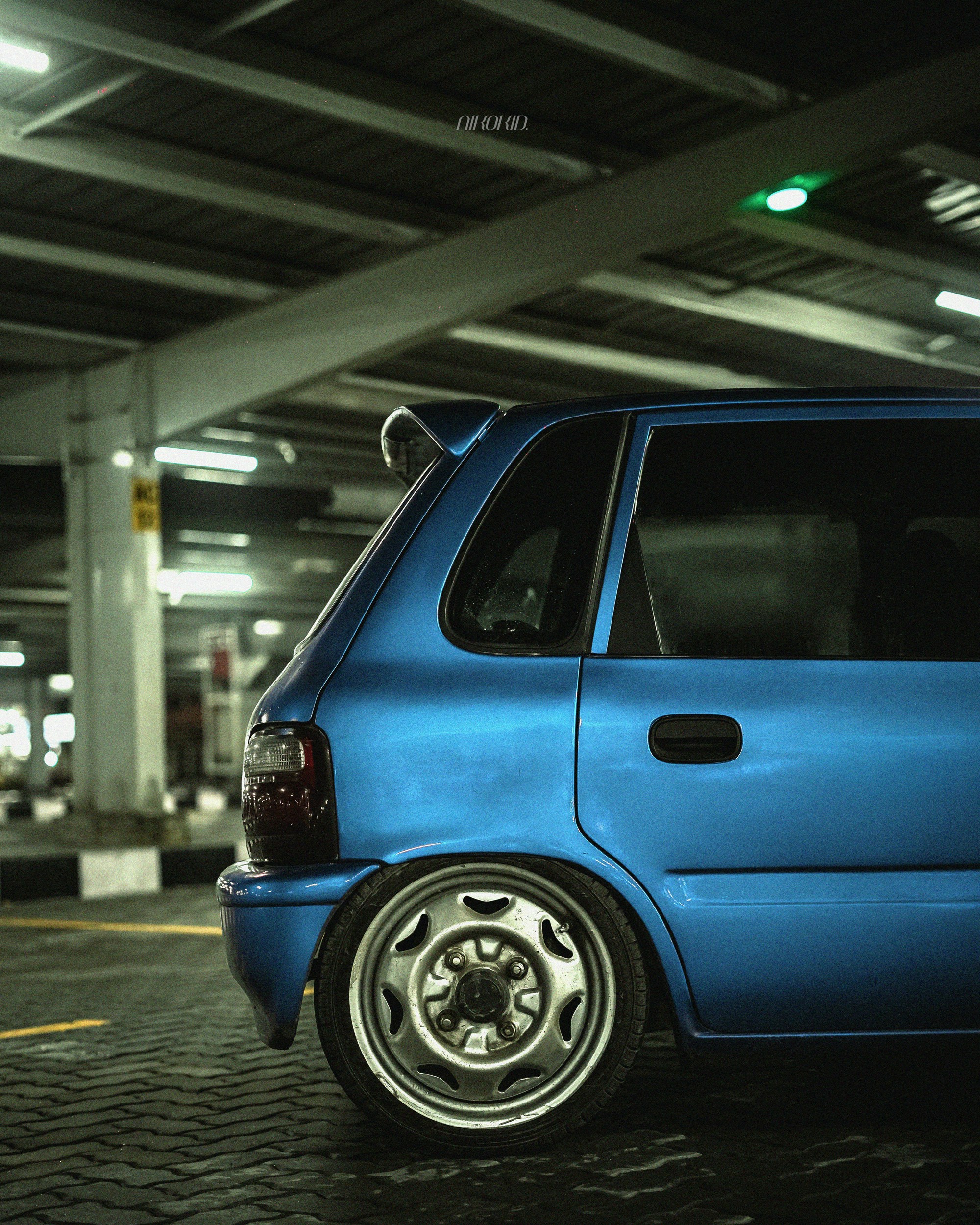 A blue car parked in a dimly lit garage.