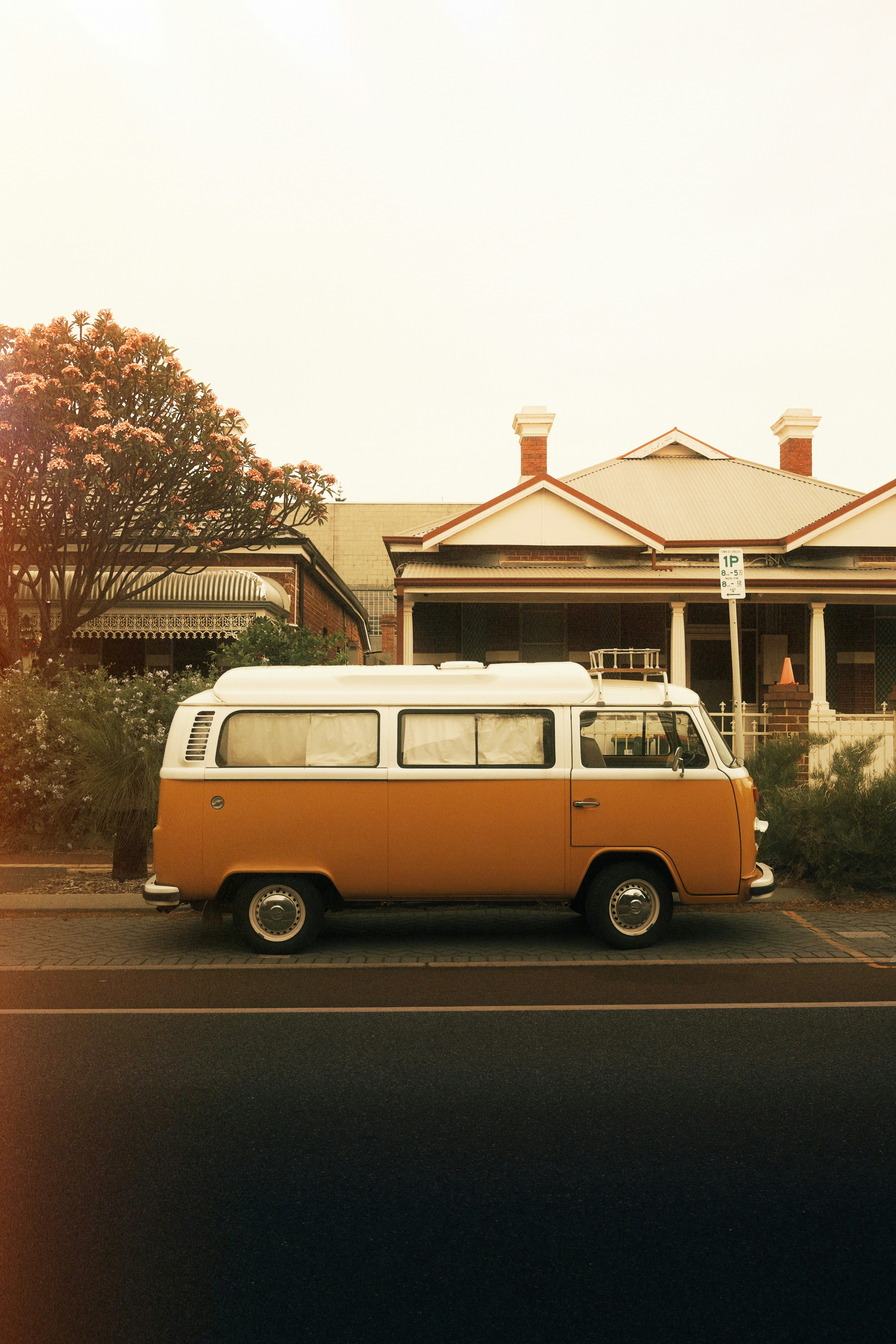 Orange and white camper van parked by a house.