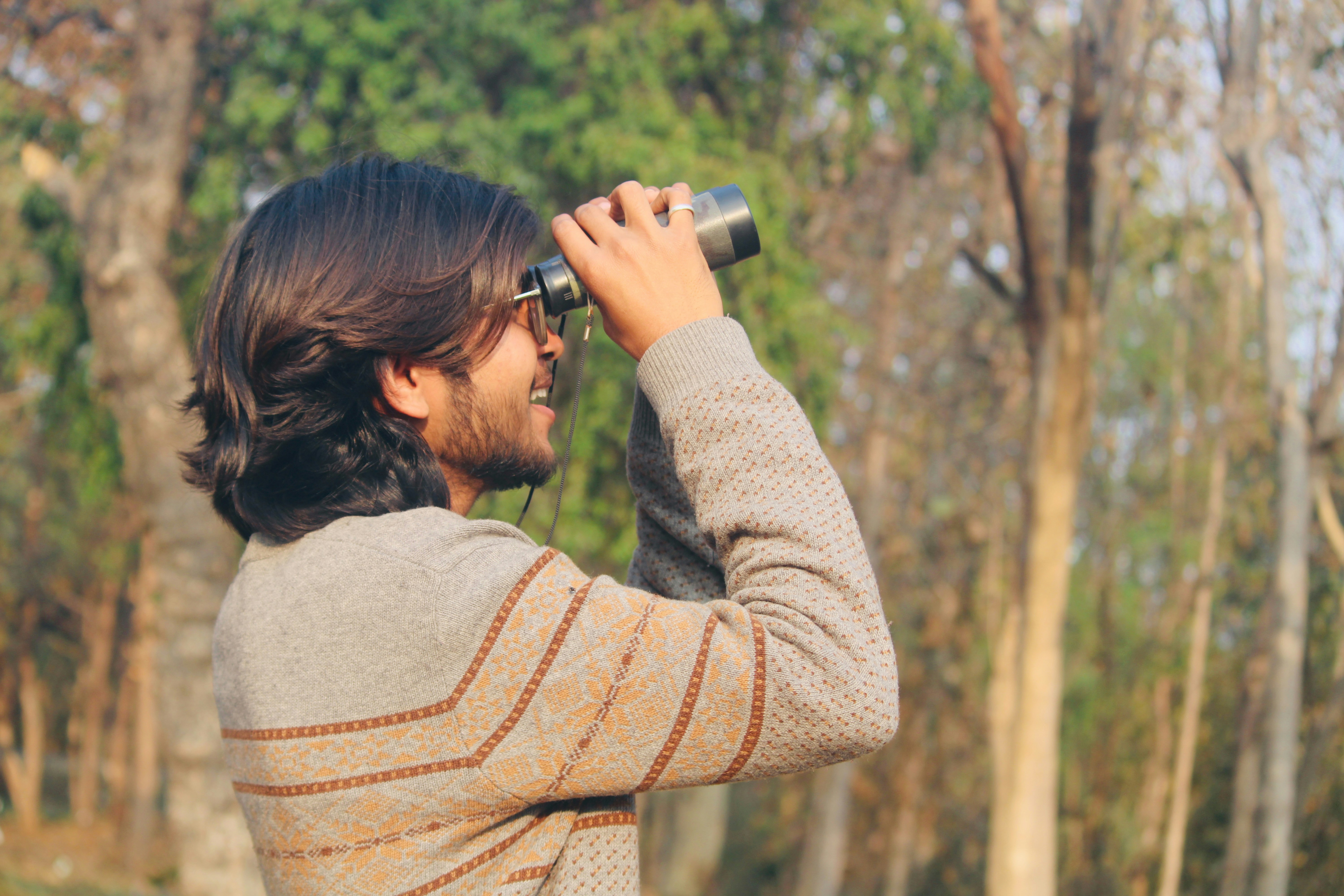 Man looking through binoculars in a forest