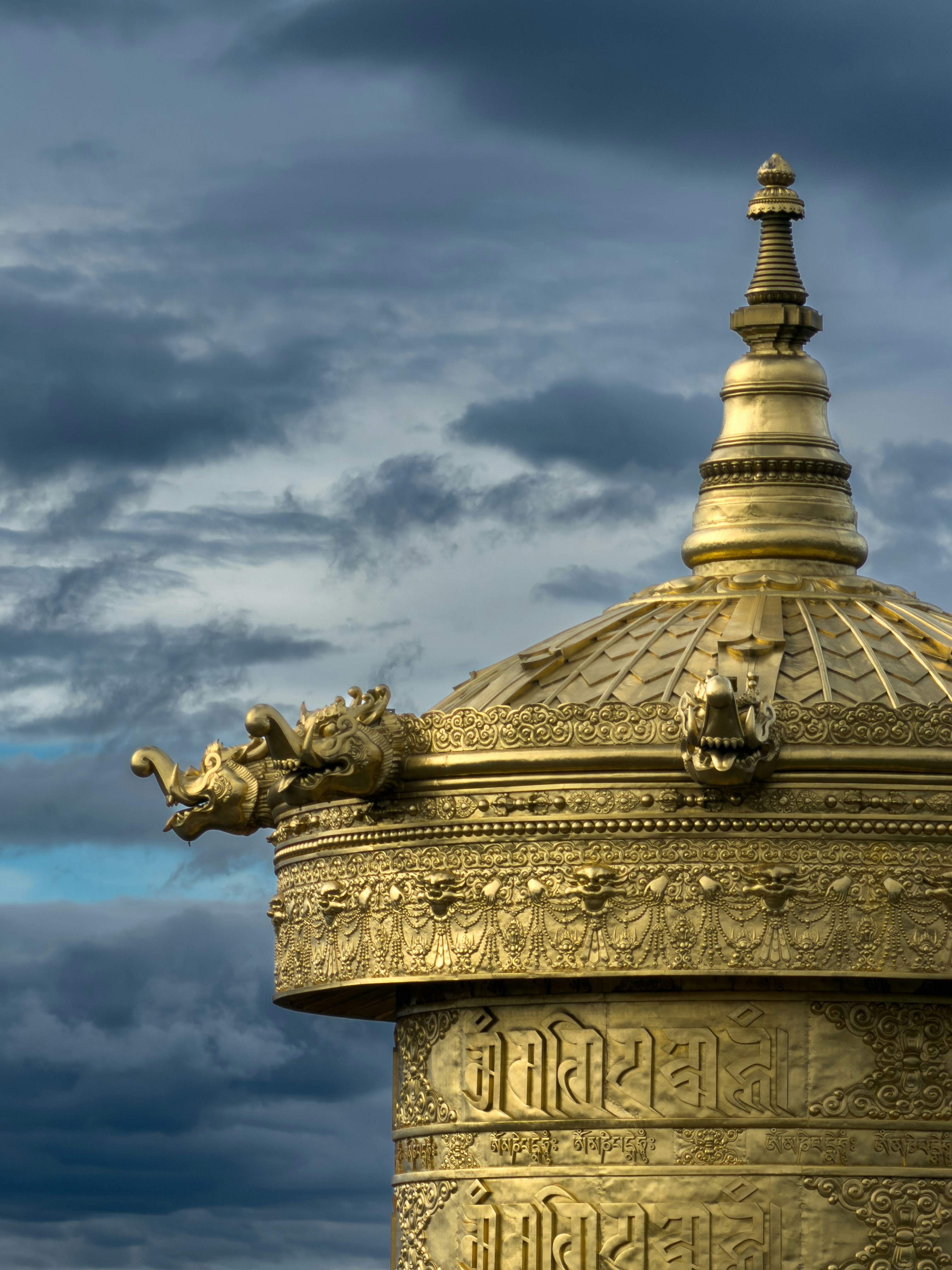 Golden prayer wheel with intricate carvings against stormy sky