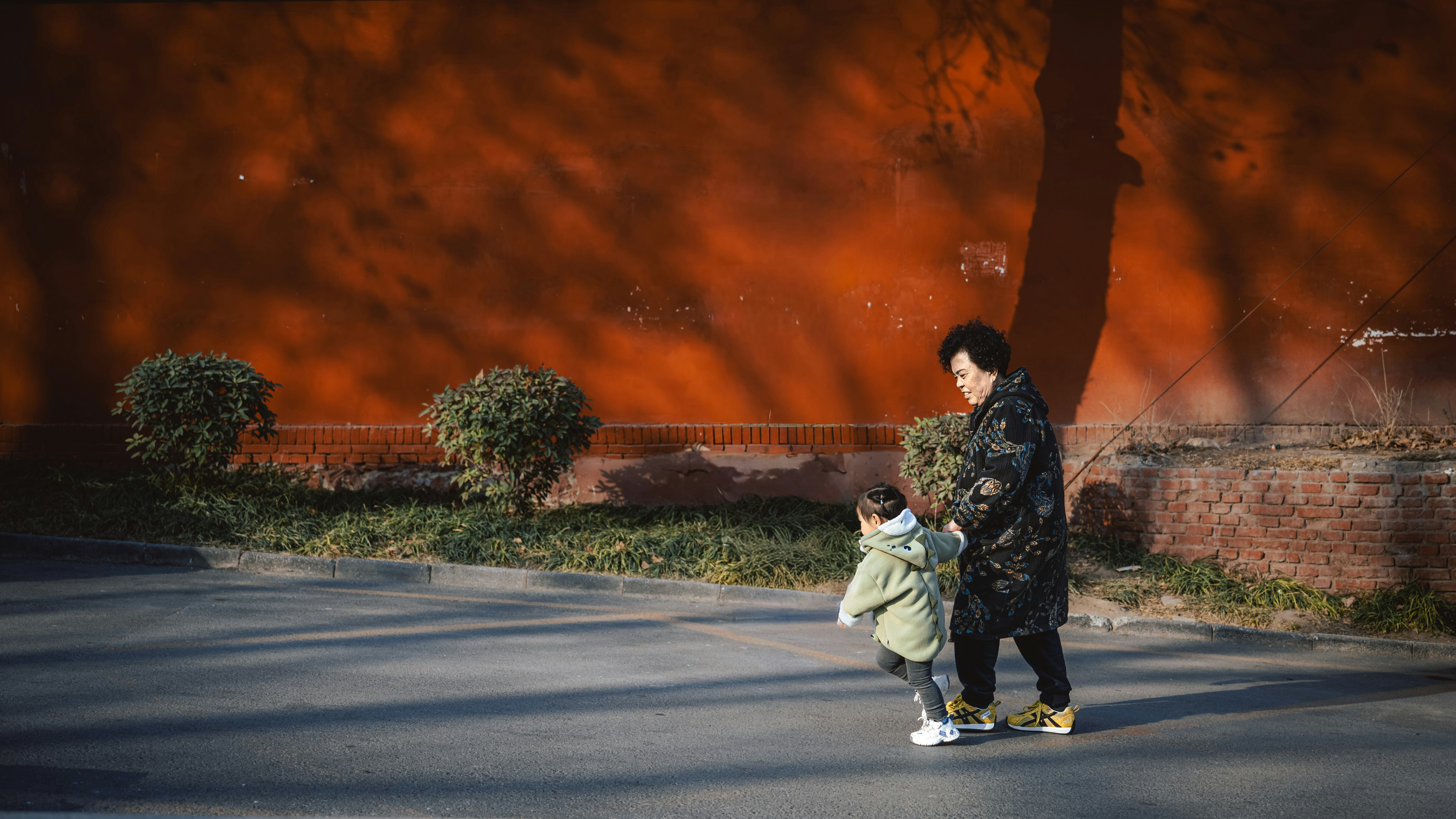 Two people walk past a textured orange wall.