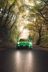 A green sports car driving on a tree-lined road.