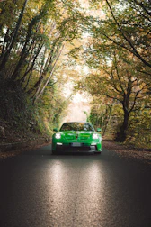 A green sports car driving on a tree-lined road.