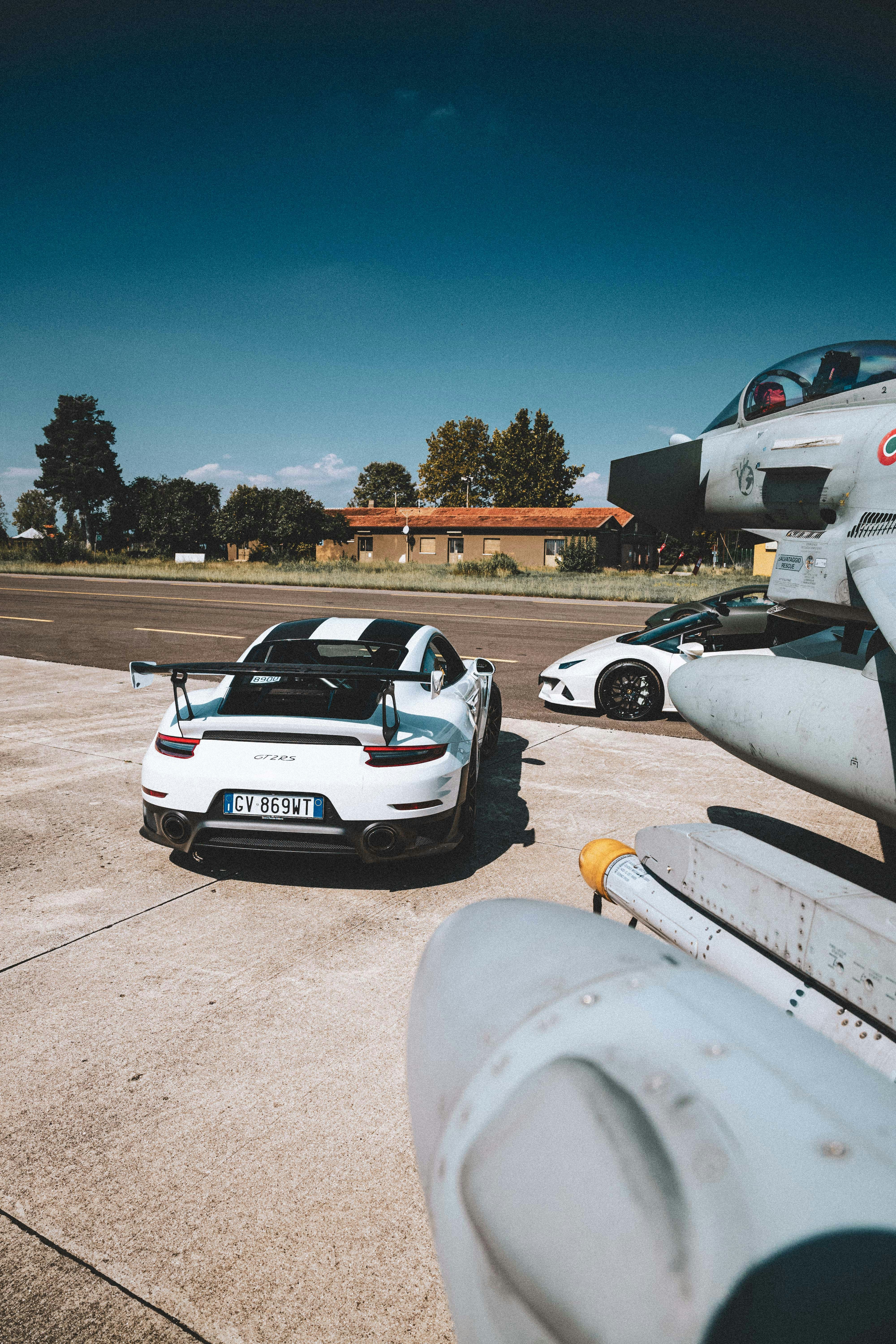 White porsche and lamborghini parked near fighter jet