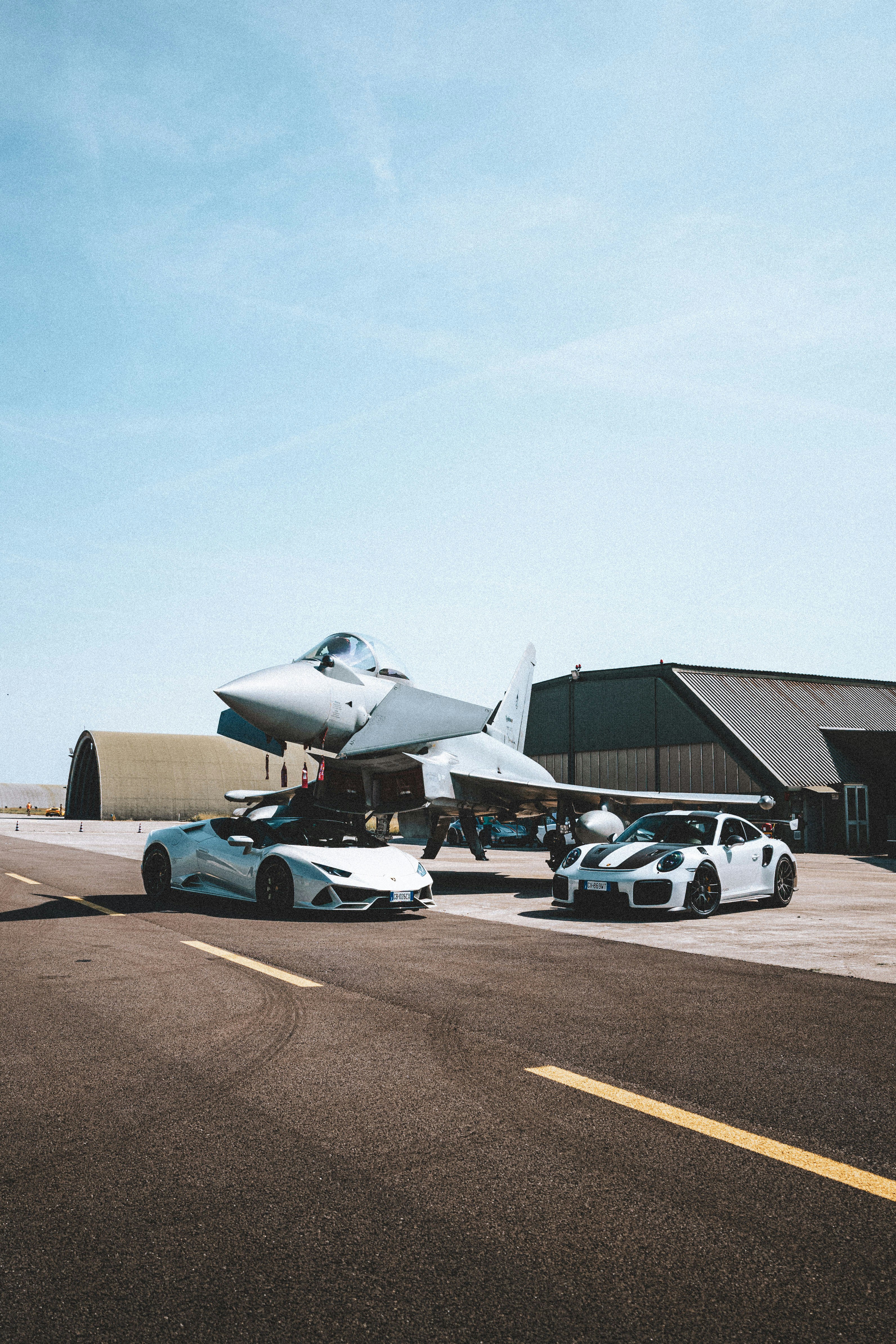 Two sports cars parked by a fighter jet