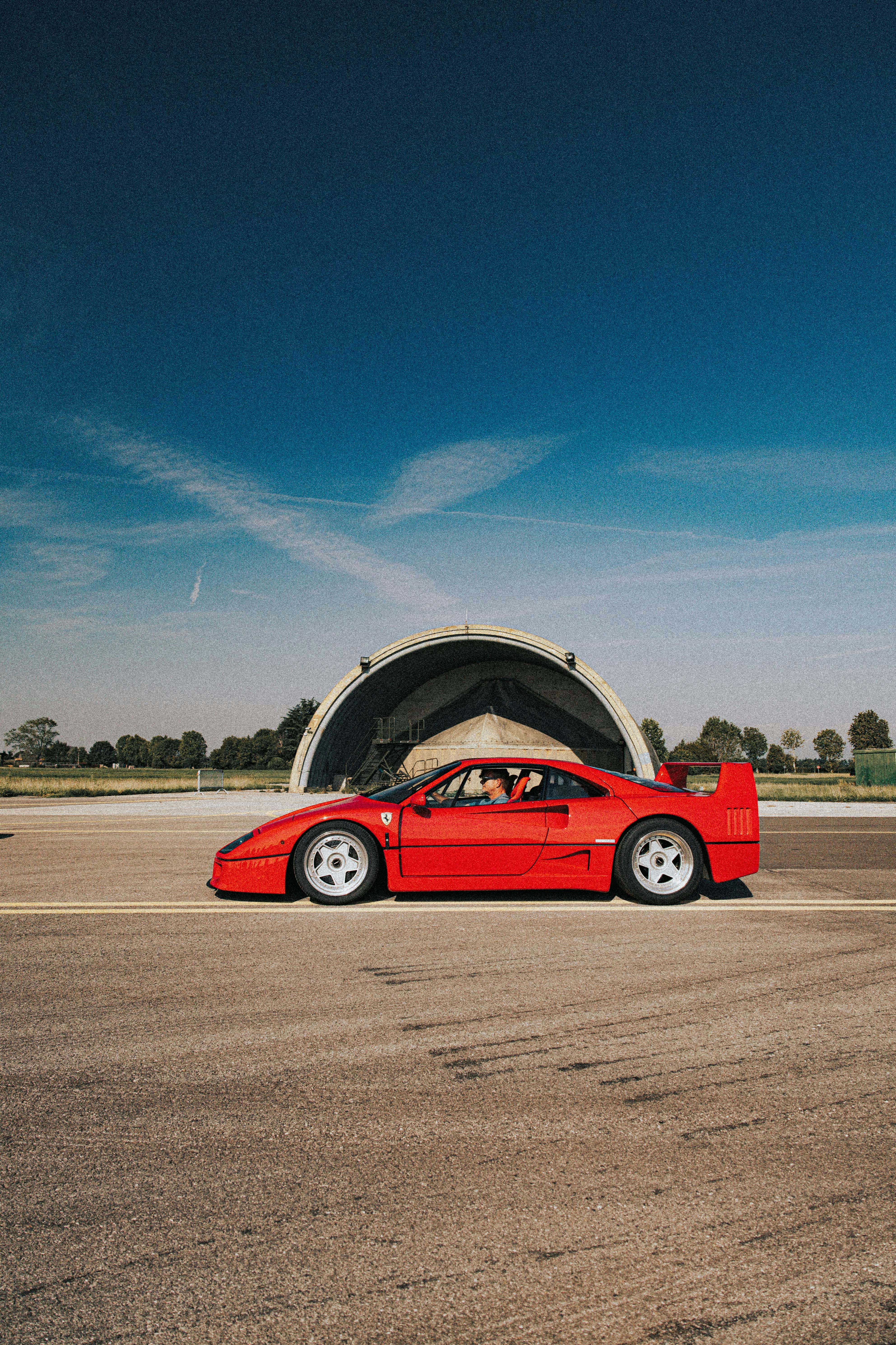Red ferrari sports car on tarmac near hangar