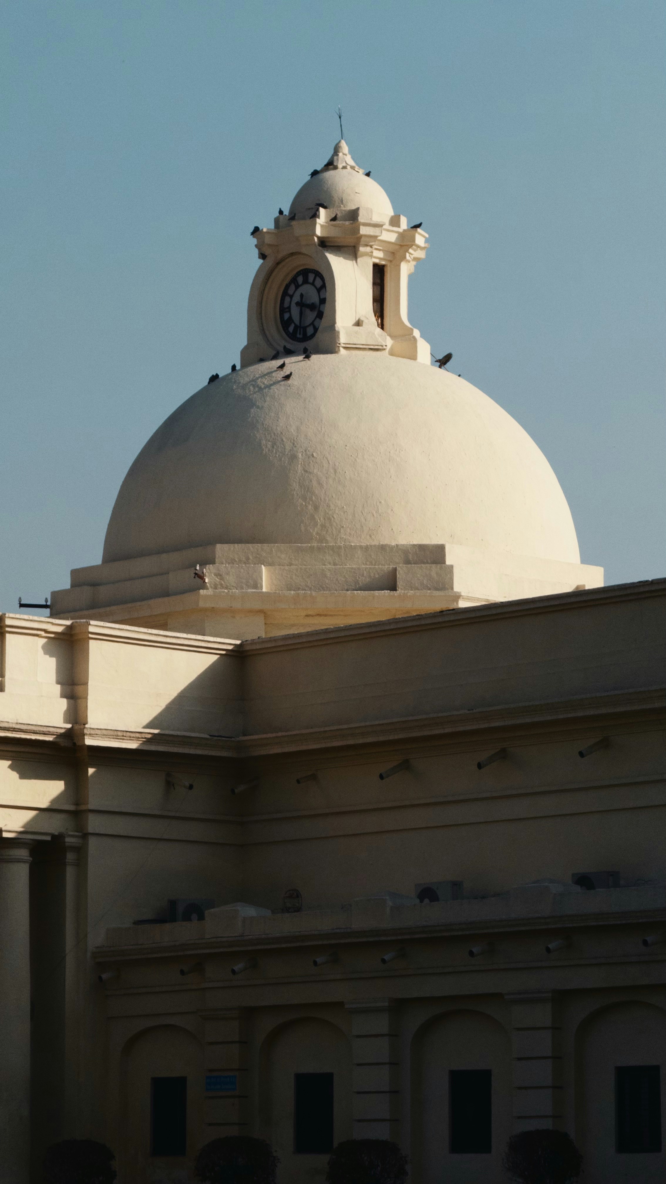 Cream colored dome with clock tower against blue sky.