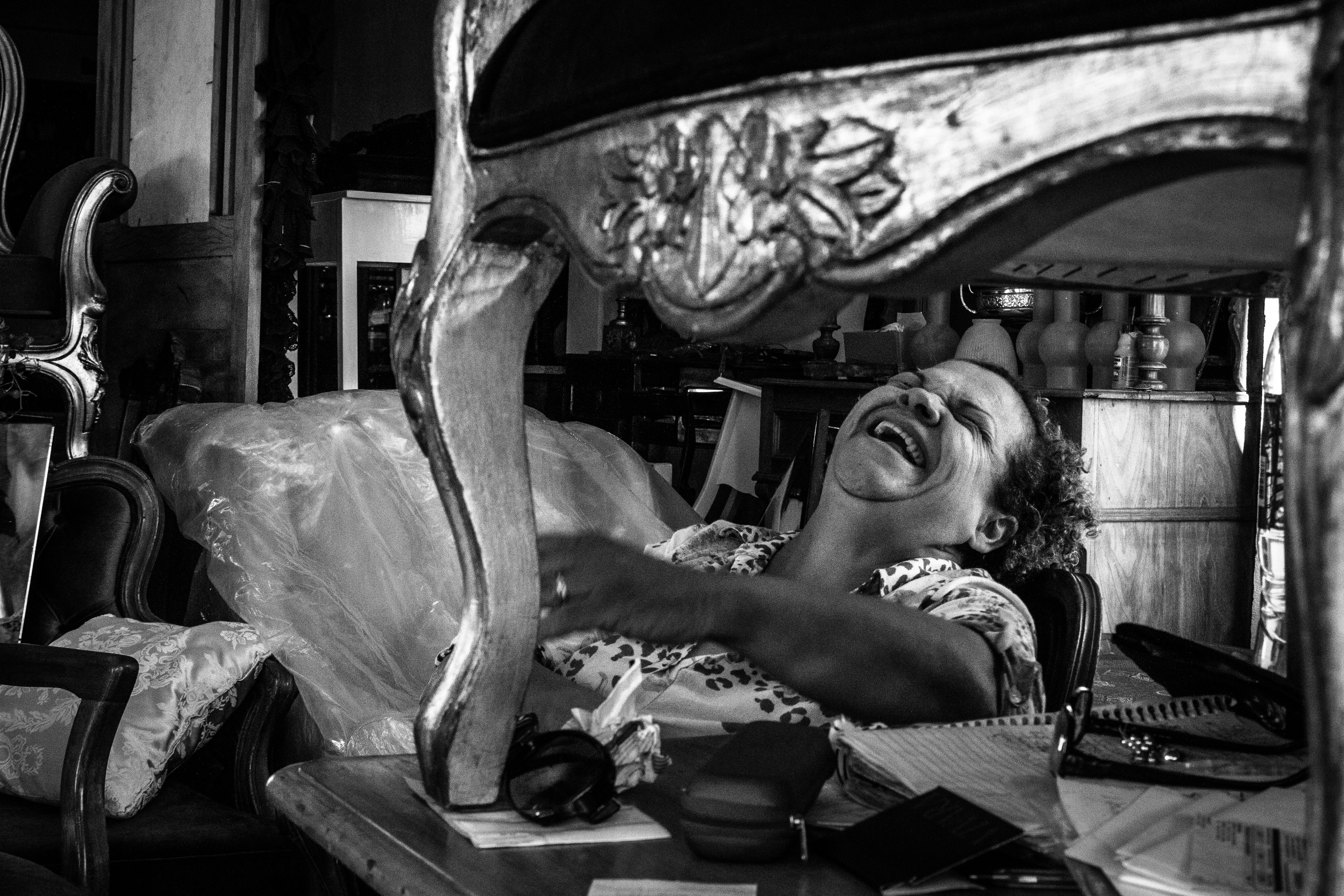 A laughing woman sits on a chair indoors.