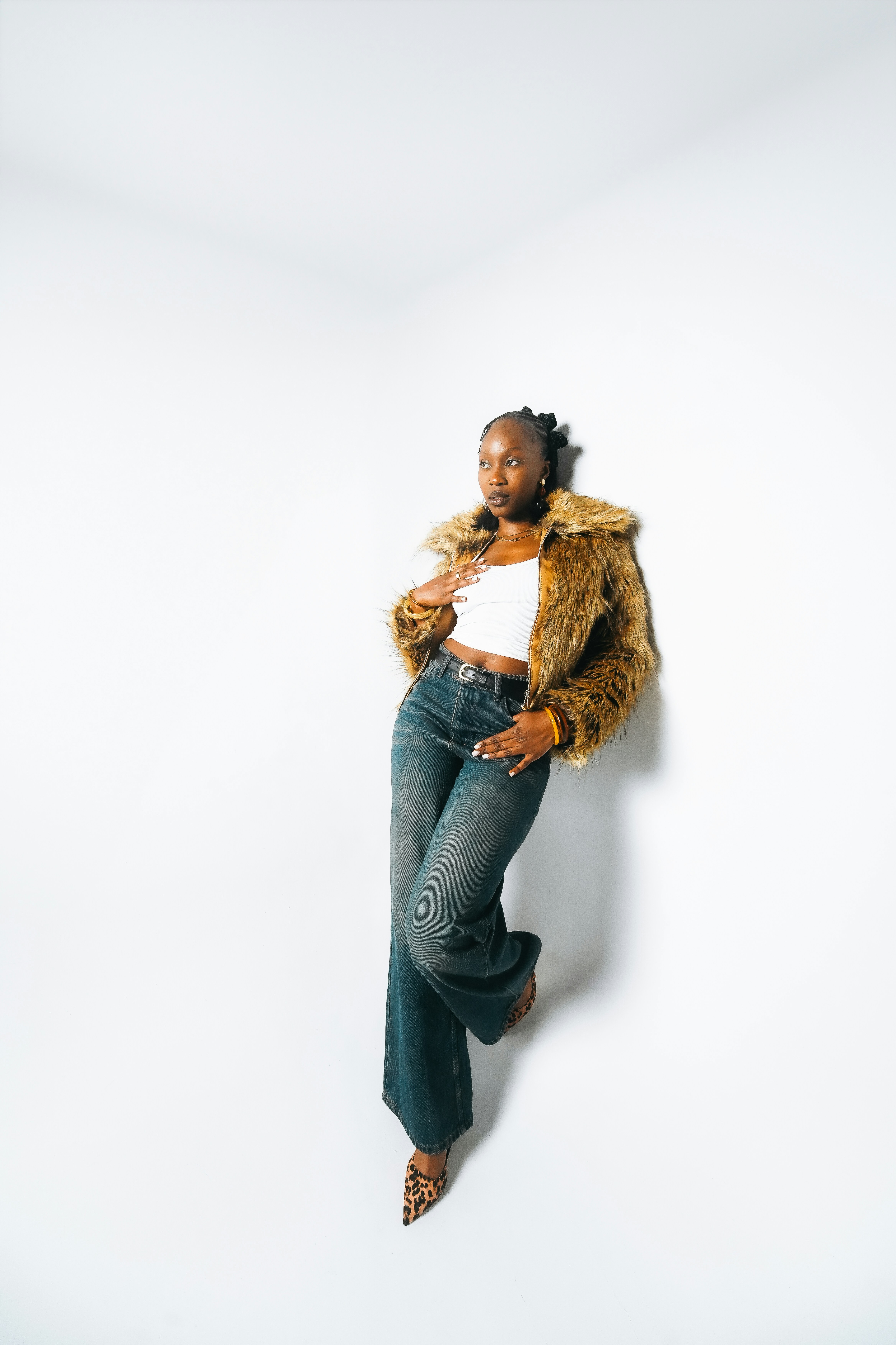 Woman in fur coat and jeans leans against wall