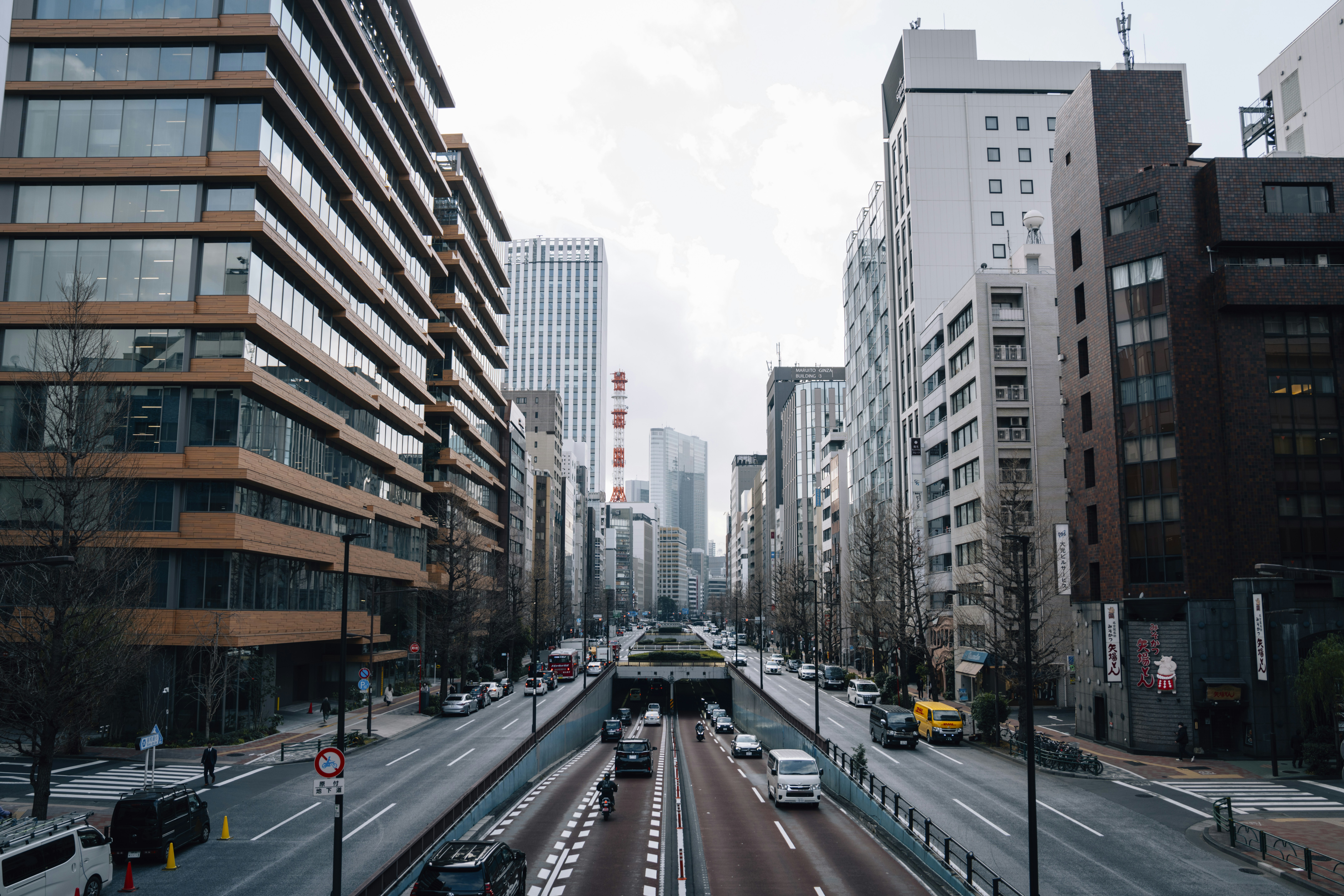 Cars driving on a wide city street with tall buildings.