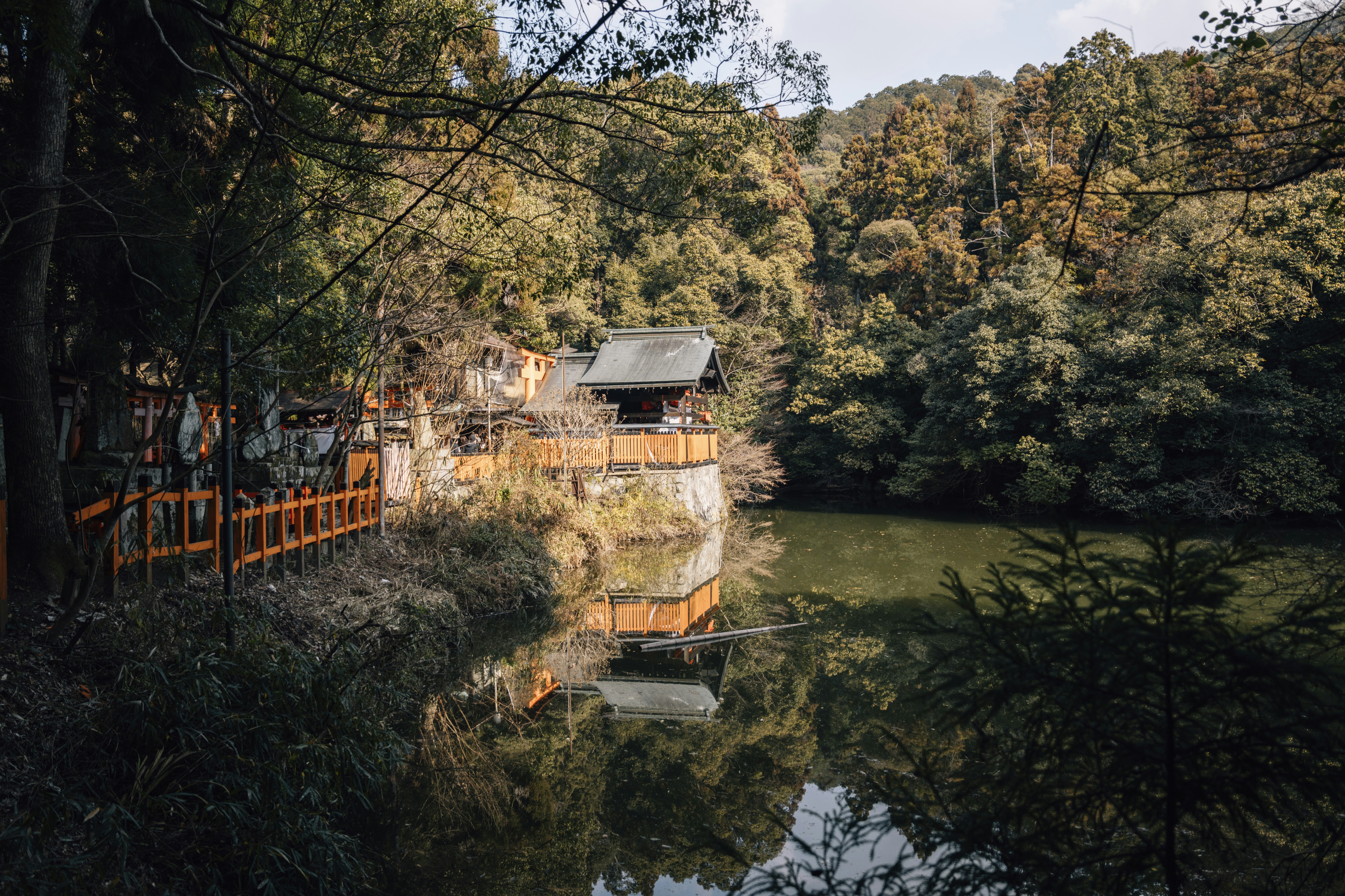 Small building beside a calm lake surrounded by trees.