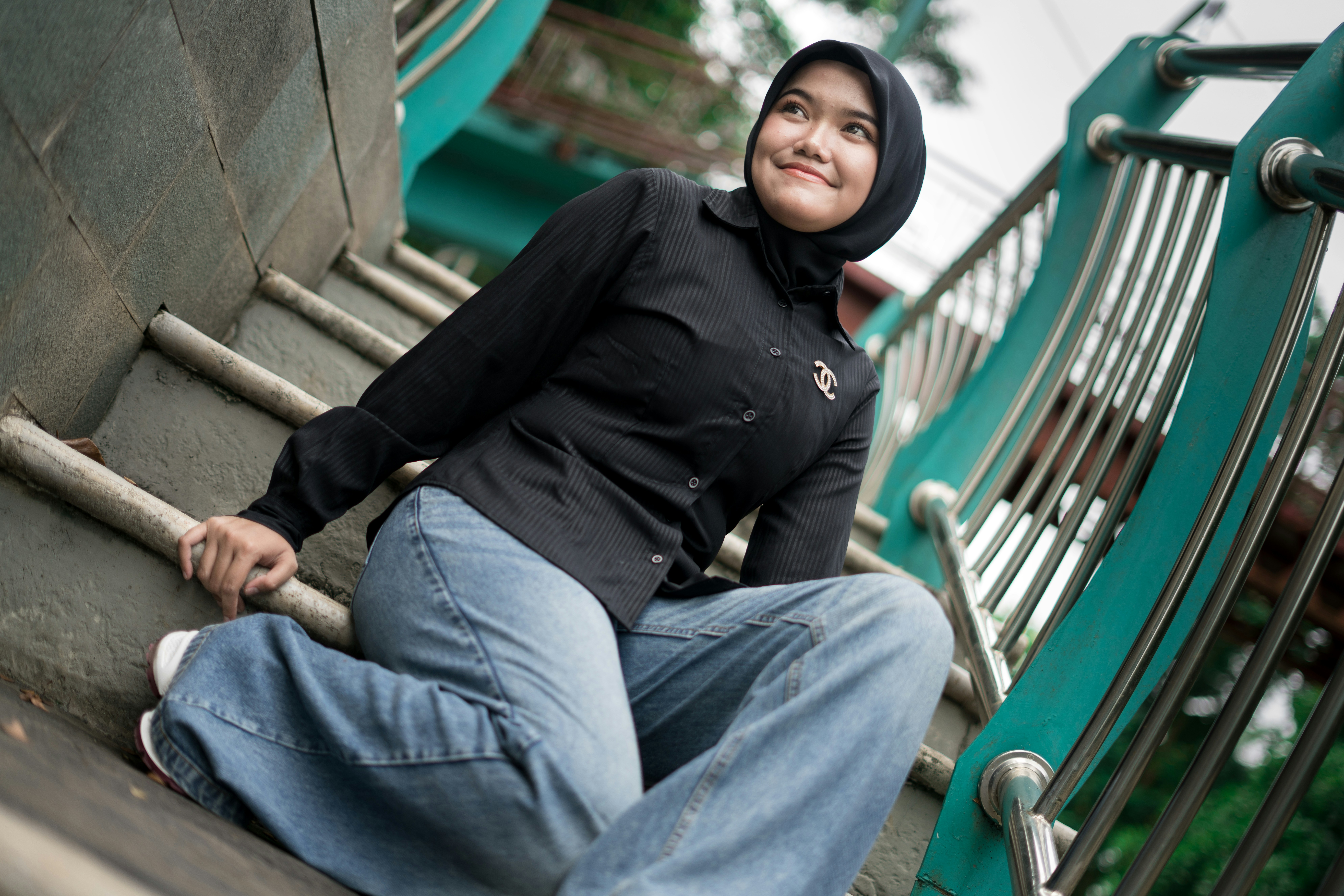 A woman in a hijab and jeans sits on stairs.