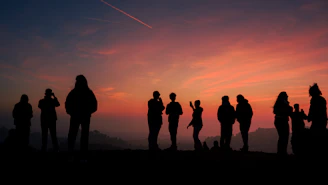 Silhouettes of people watching a vibrant sunset over hills