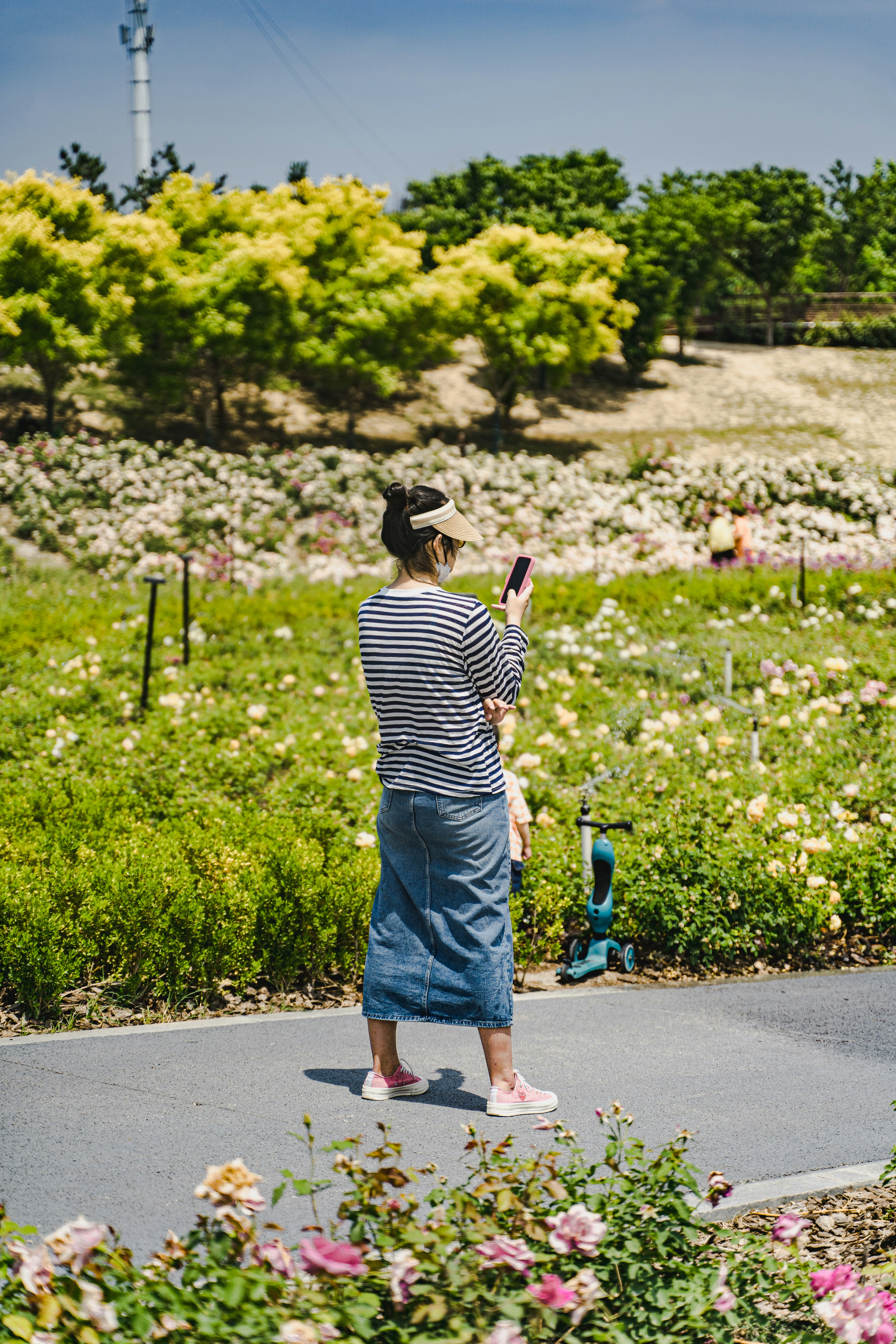Frau im Jeansrock macht ein Foto im Blumengarten