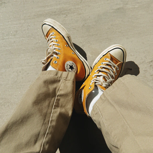 A person in tan pants wearing a pair of orange Converse sneakers