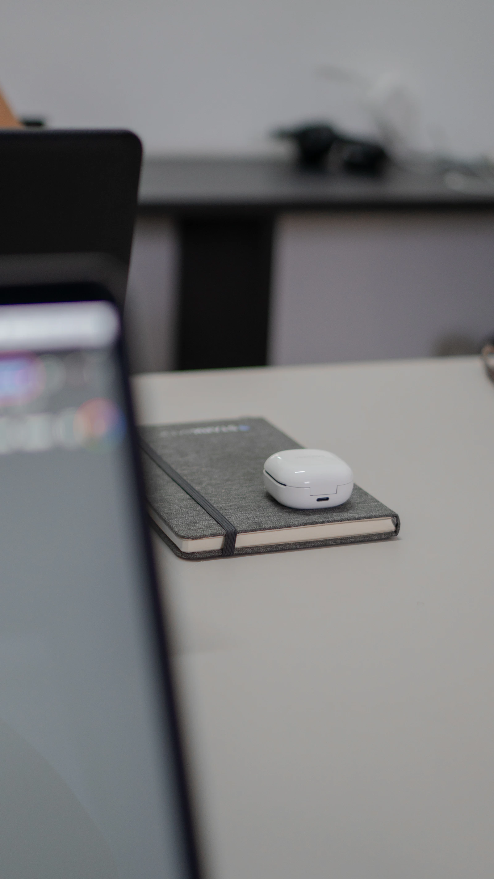 Wireless earbuds resting on a notebook beside a laptop
