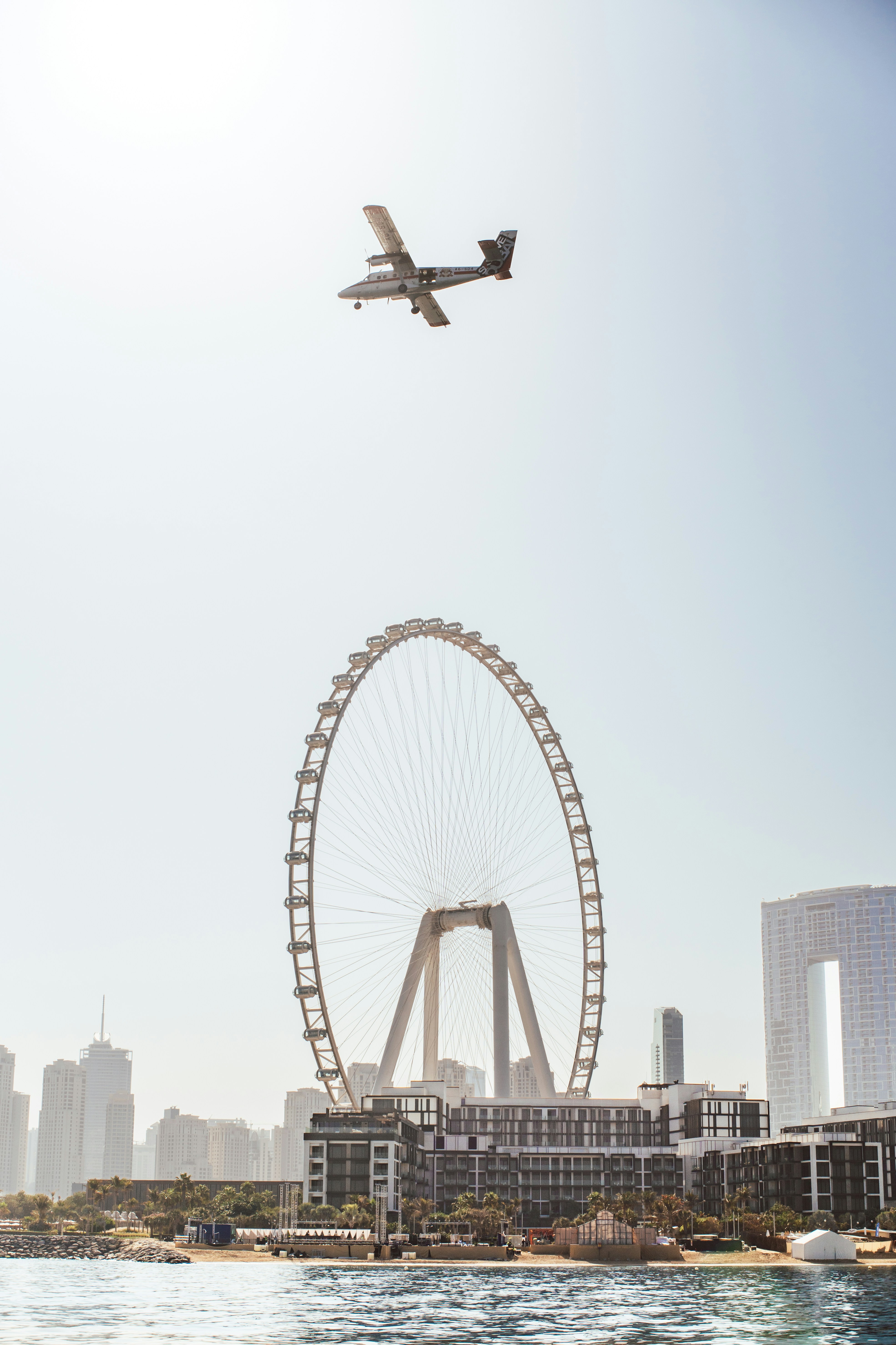 A small airplane flies over a large ferris wheel.