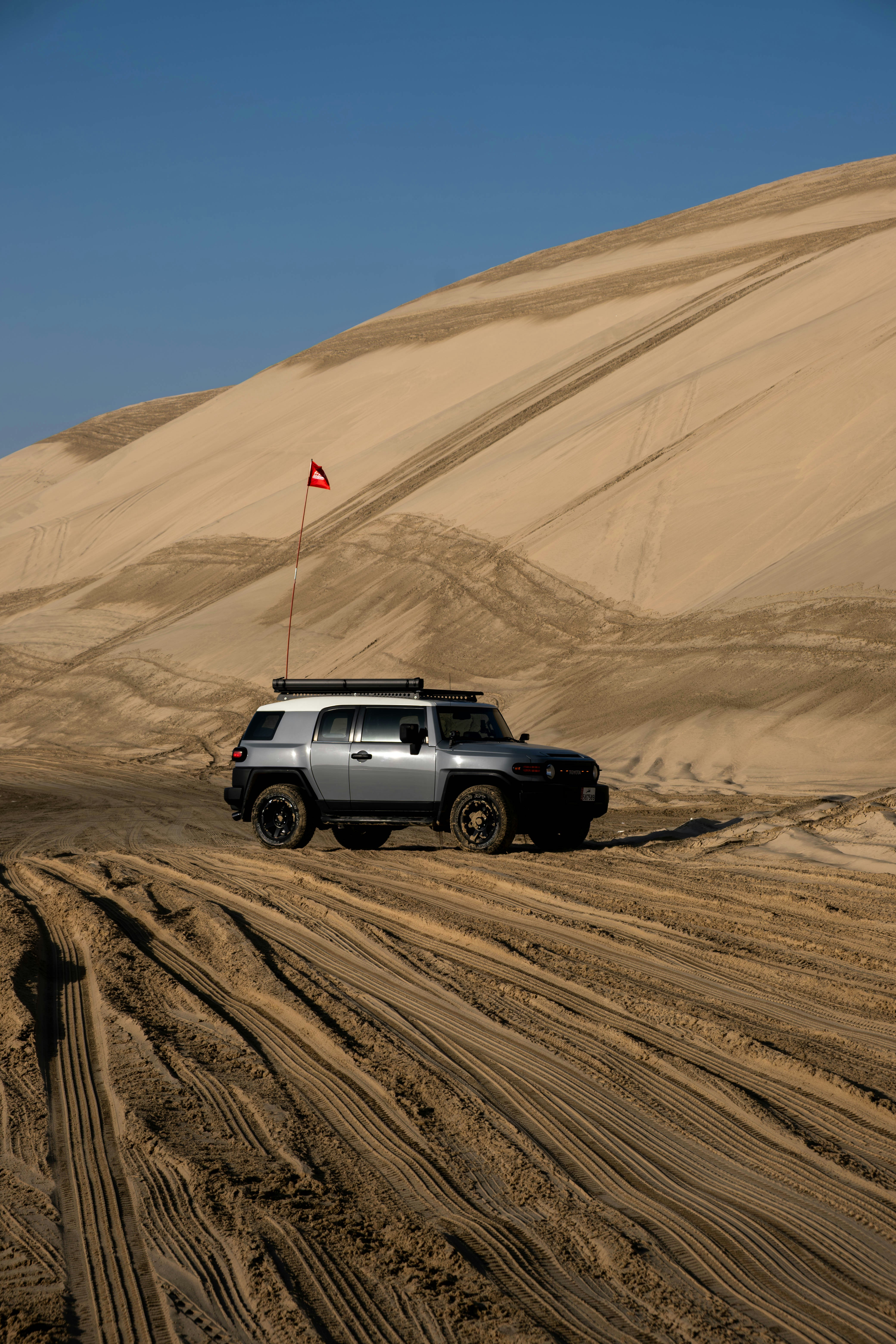 Silver suv driving on sand dunes with tracks.