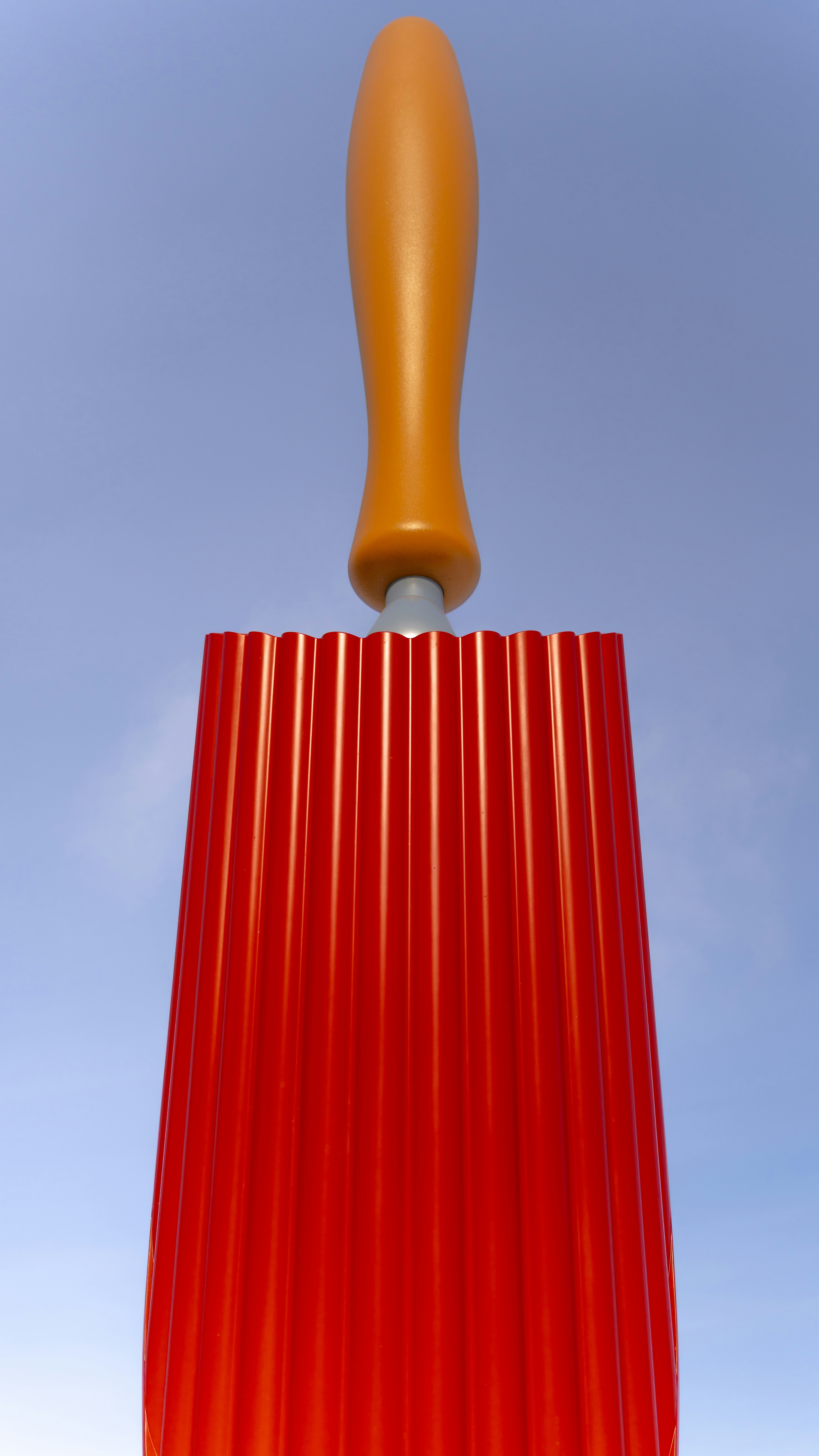 A red fluted object with an orange handle against sky
