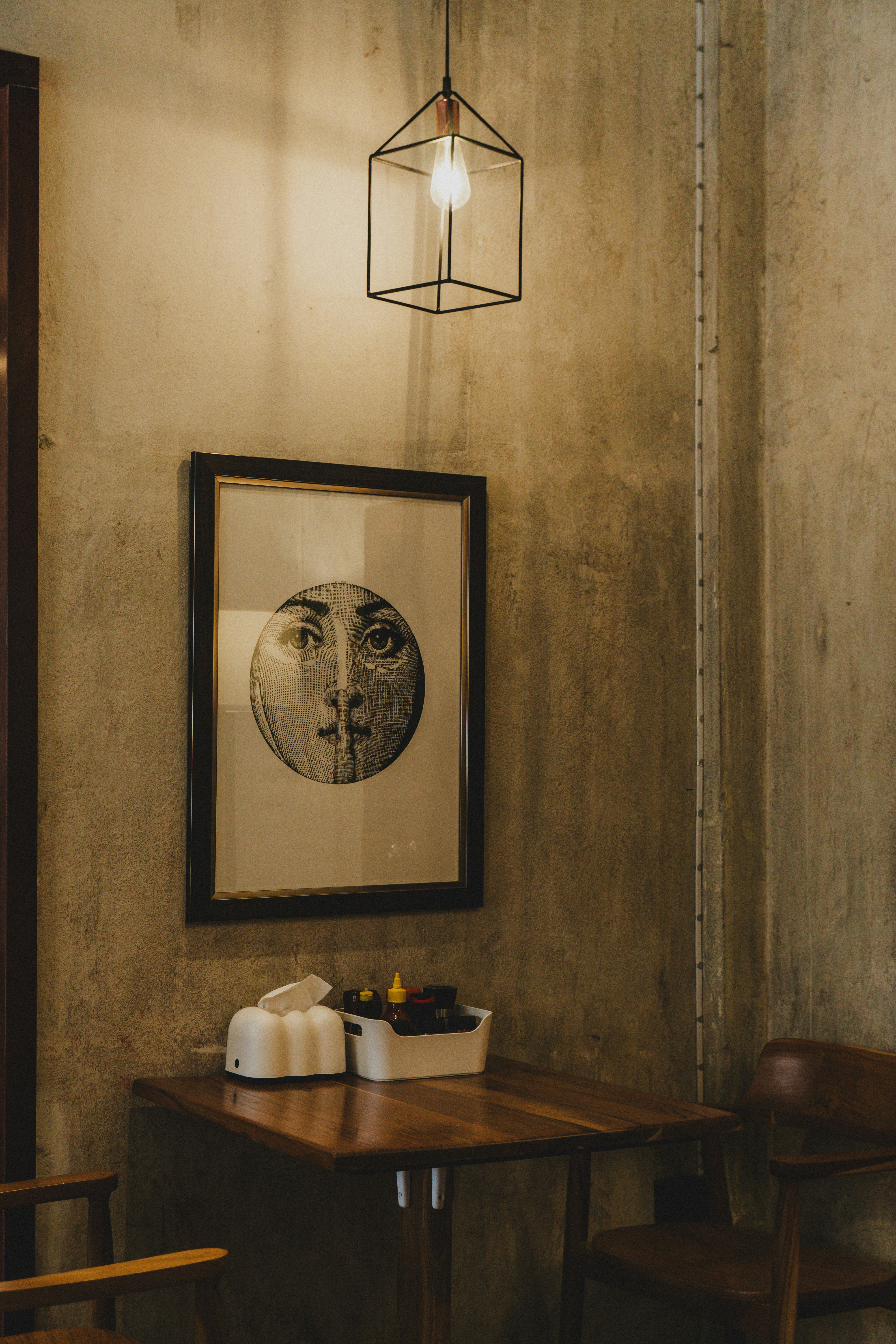 Framed artwork of a face hangs above a table.
