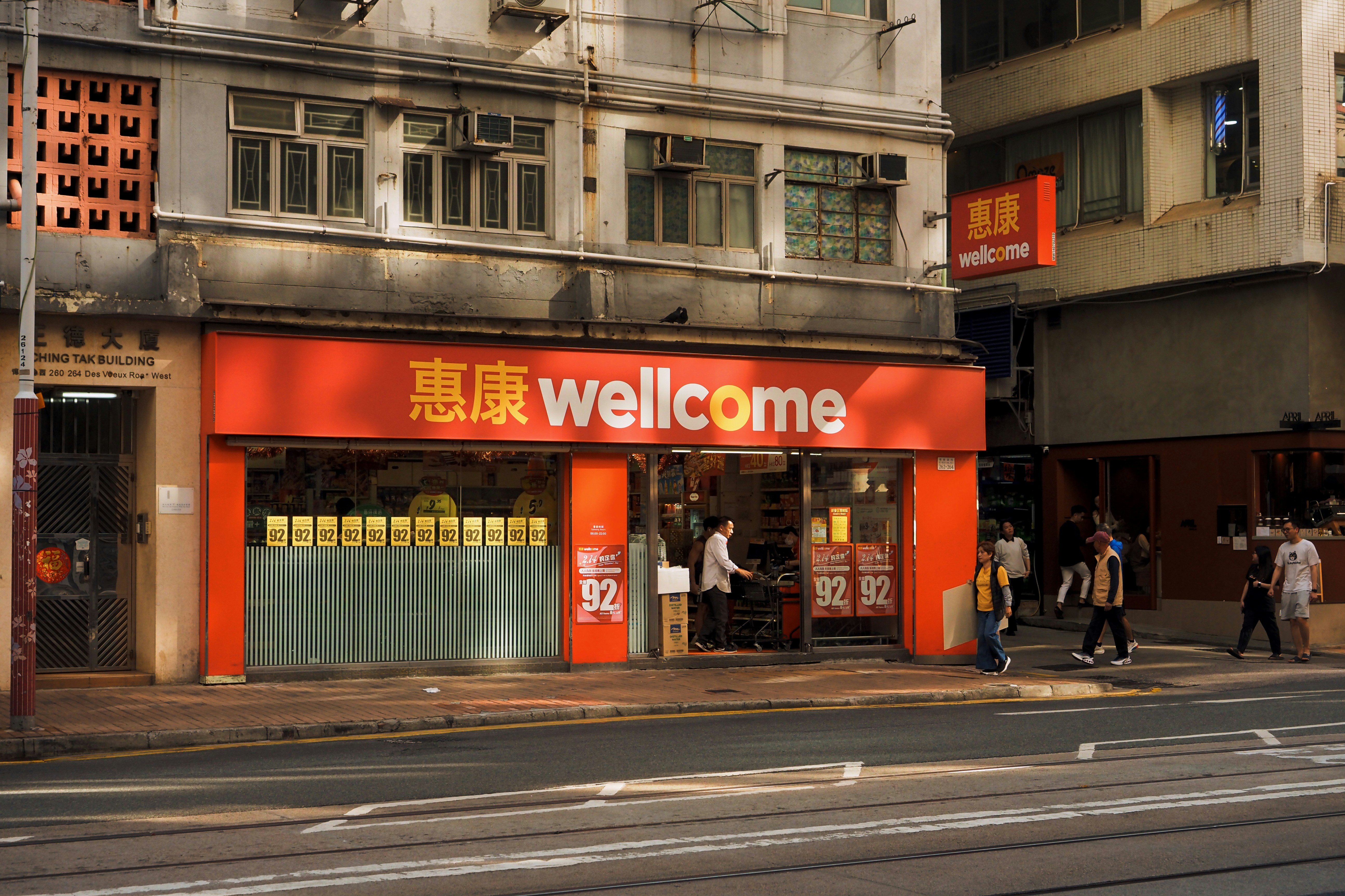 A bright orange "wellcome" supermarket storefront on a city street.