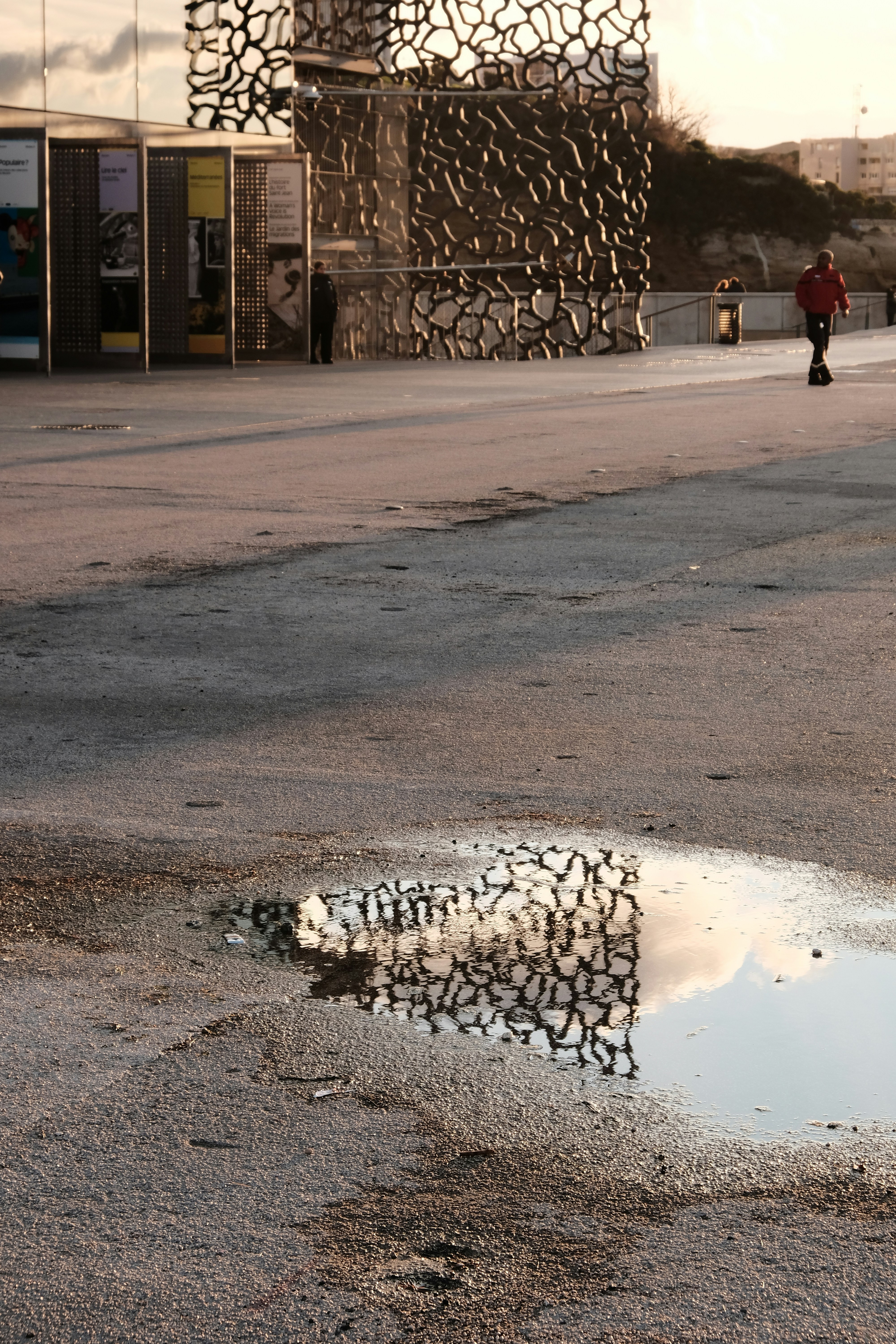 Puddle reflects modern building and cloudy sky