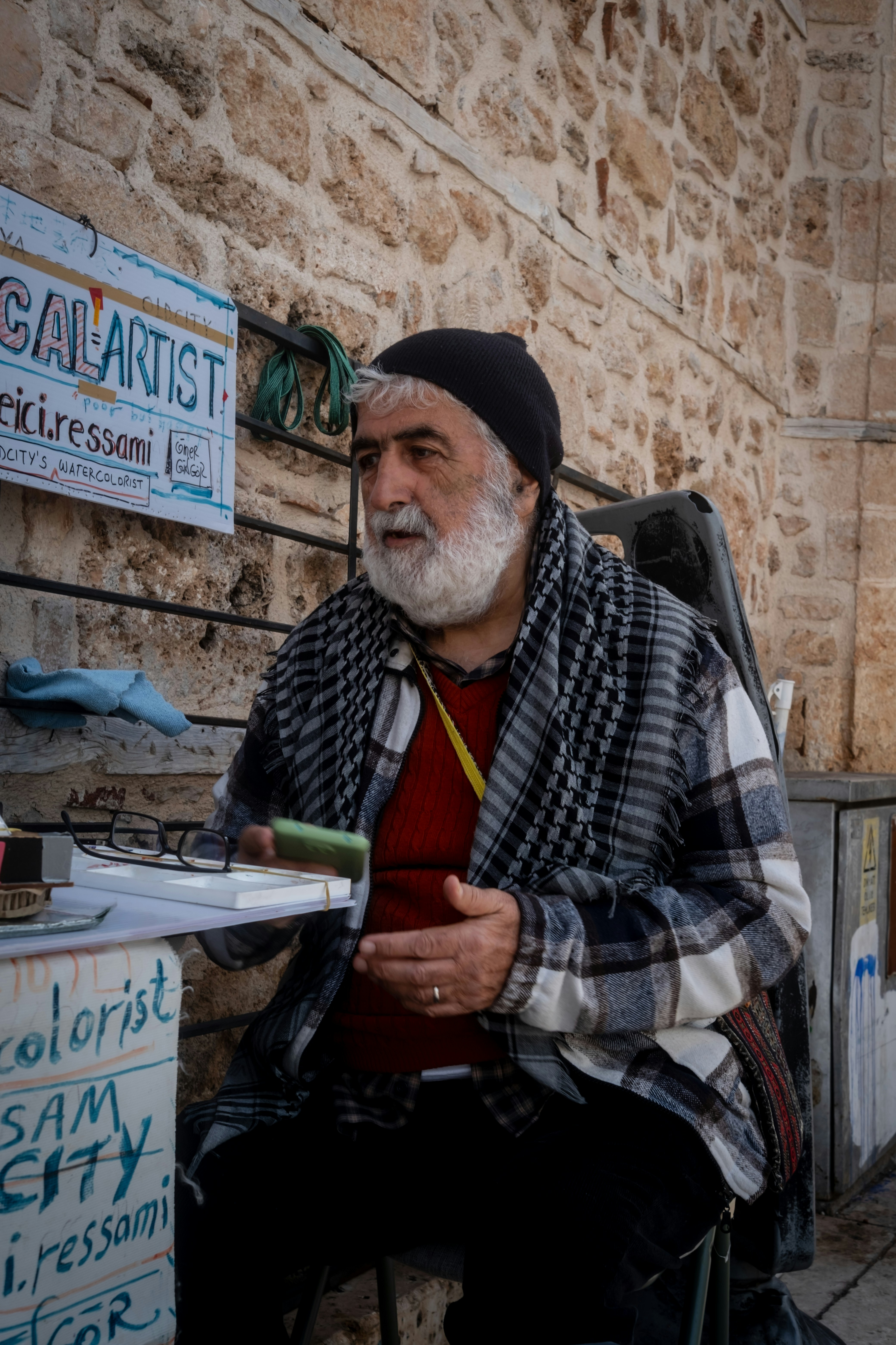An artist with a beard and beanie sits outside.