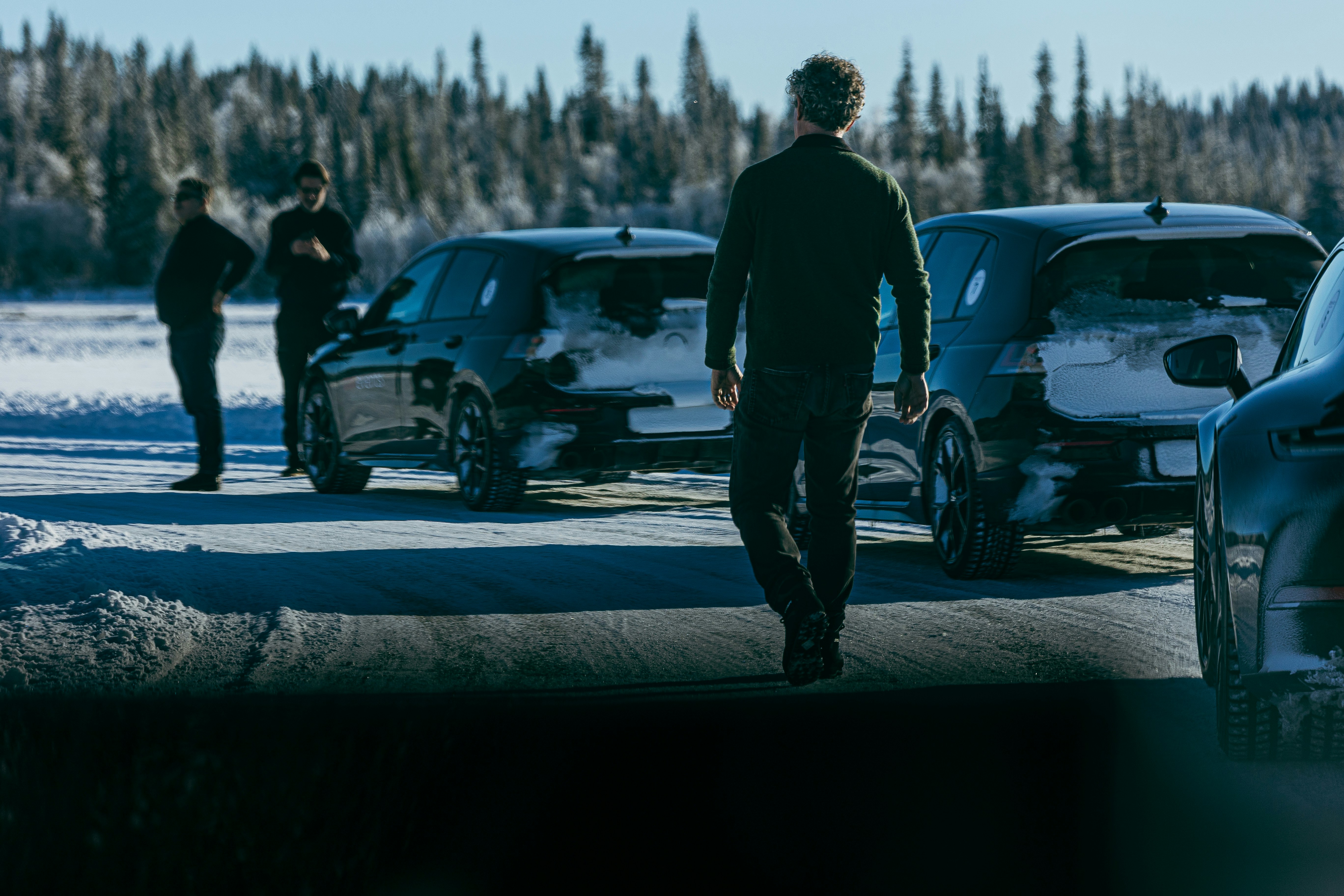 Men stand near cars in a snowy, wooded area.