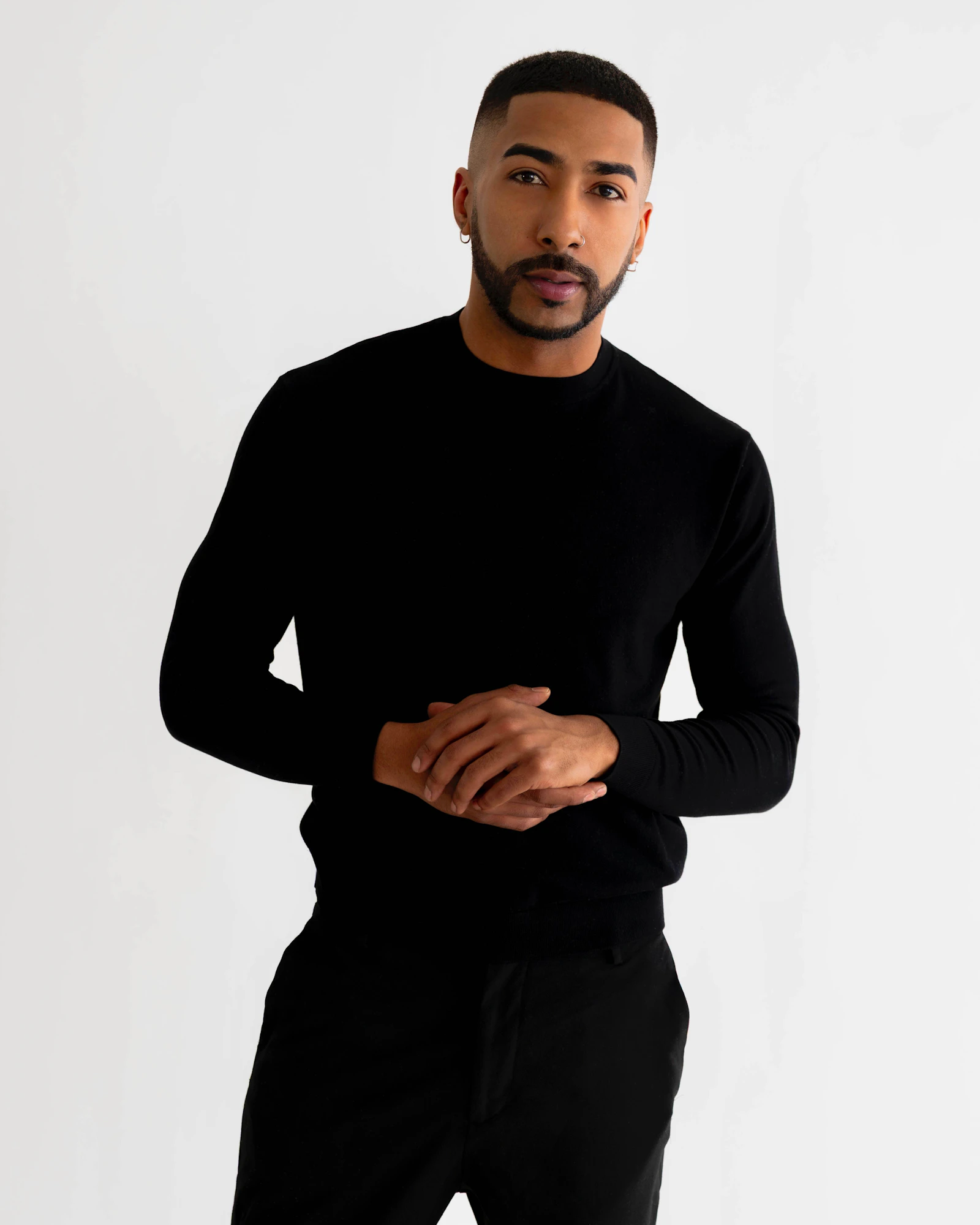 Retrato de estudio de un hombre con jersey y pantalones negros y las manos juntas