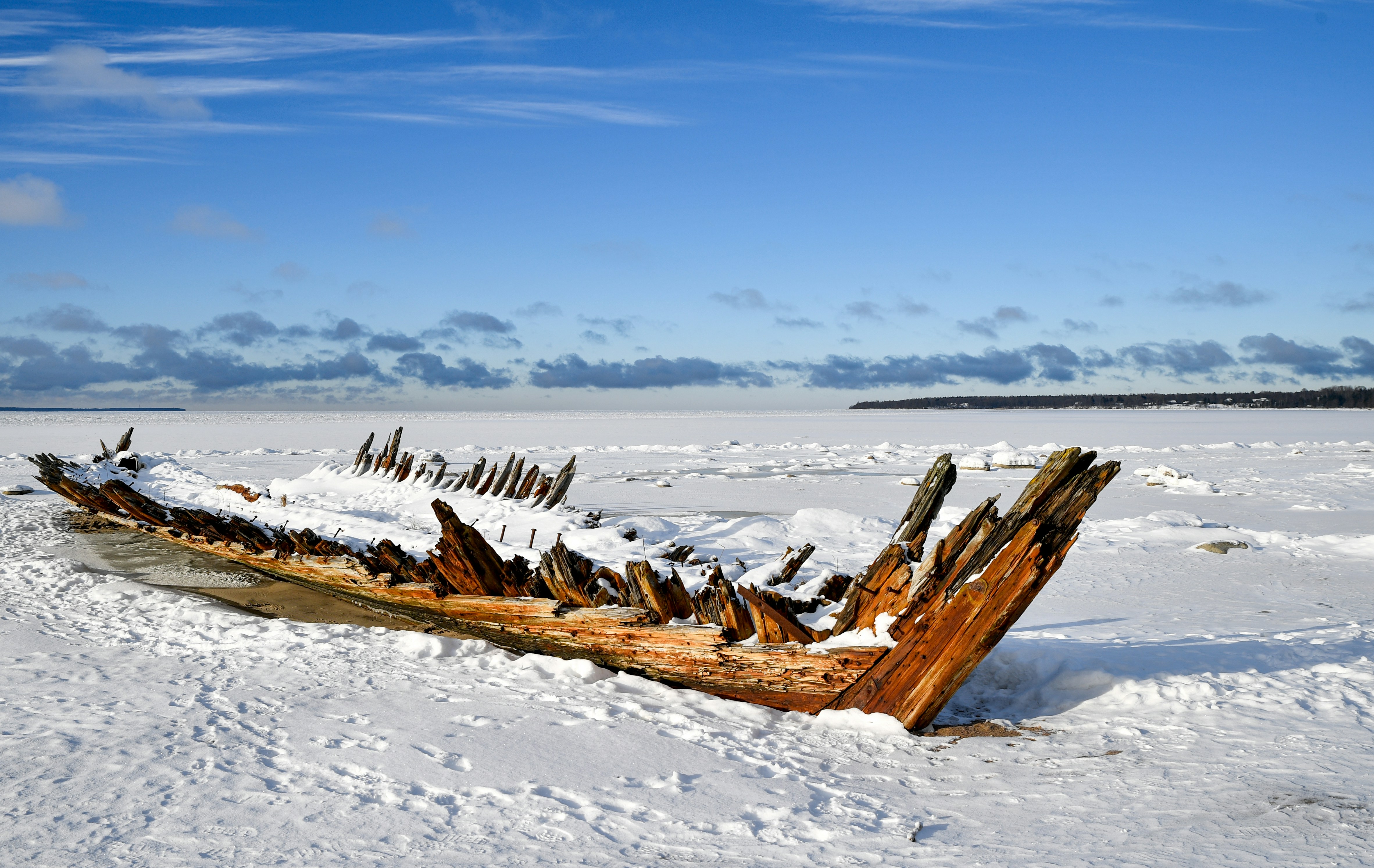 Wrecked wooden boat covered in snow on frozen shore