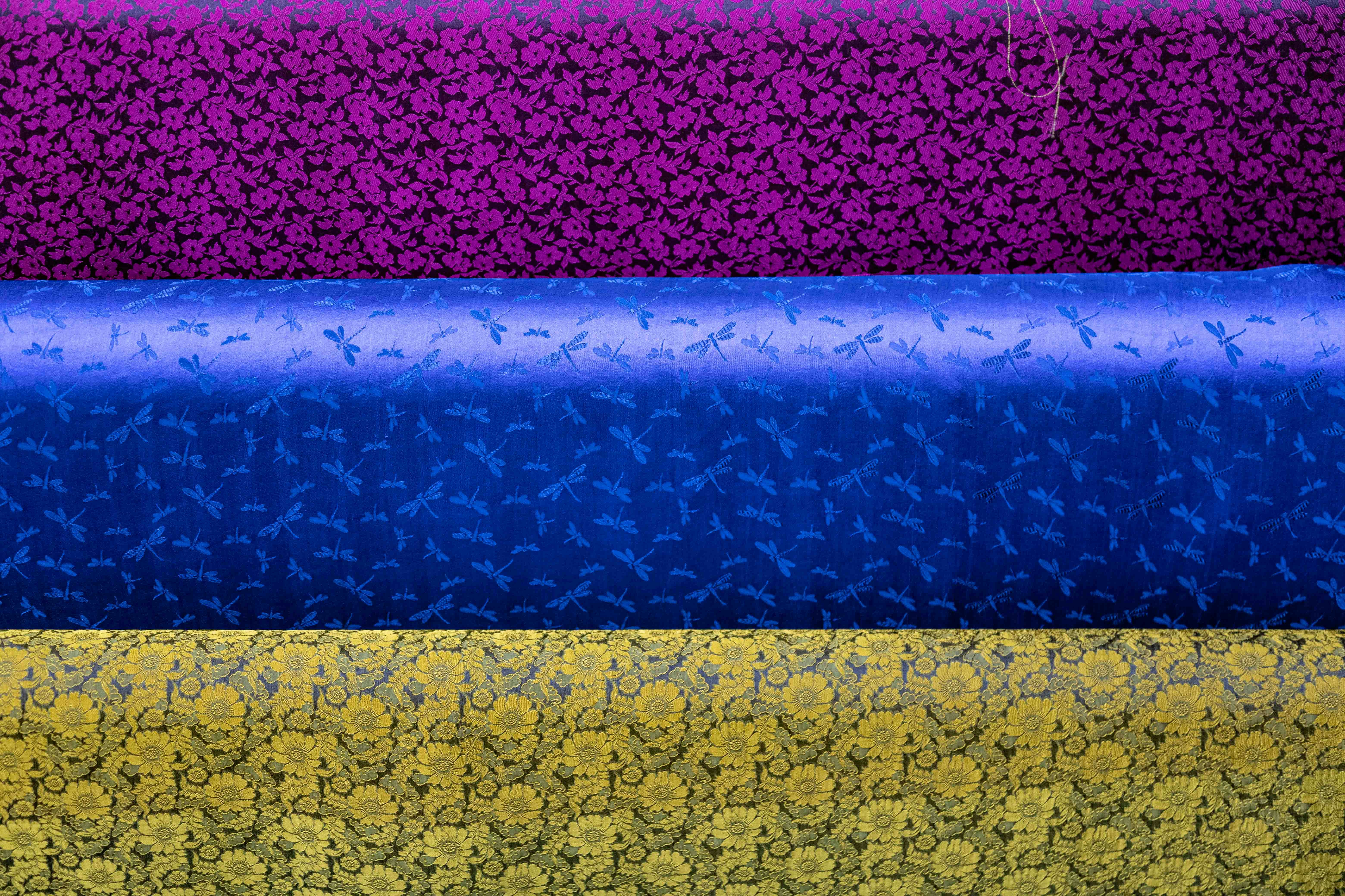 Three rolls of patterned fabric in purple, blue, and yellow