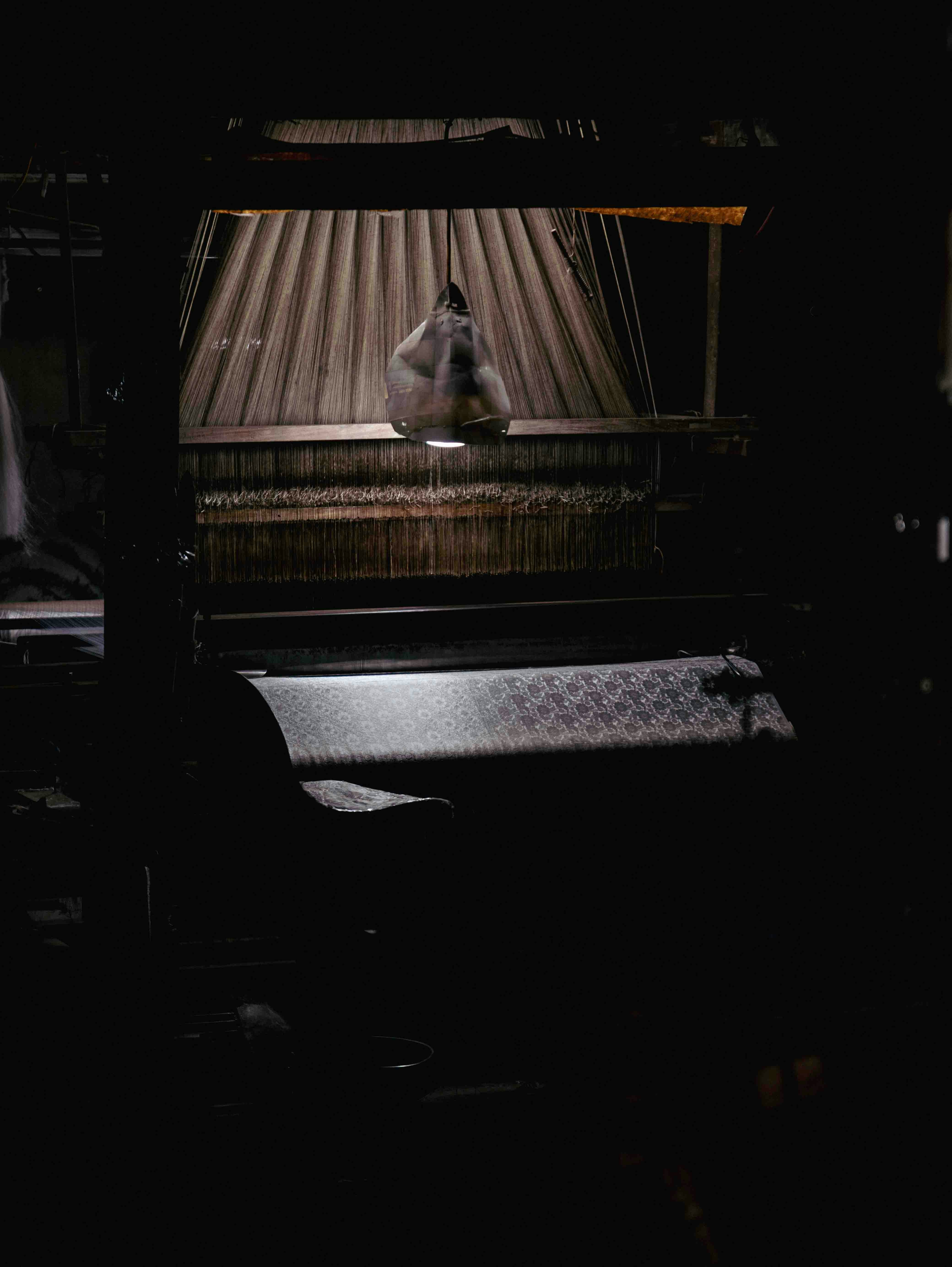 A dimly lit loom with fabric being woven
