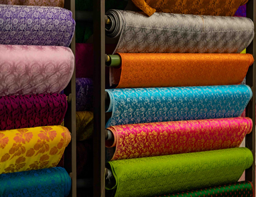 Rolls of patterned fabric stacked on the shelves of a textile shop.