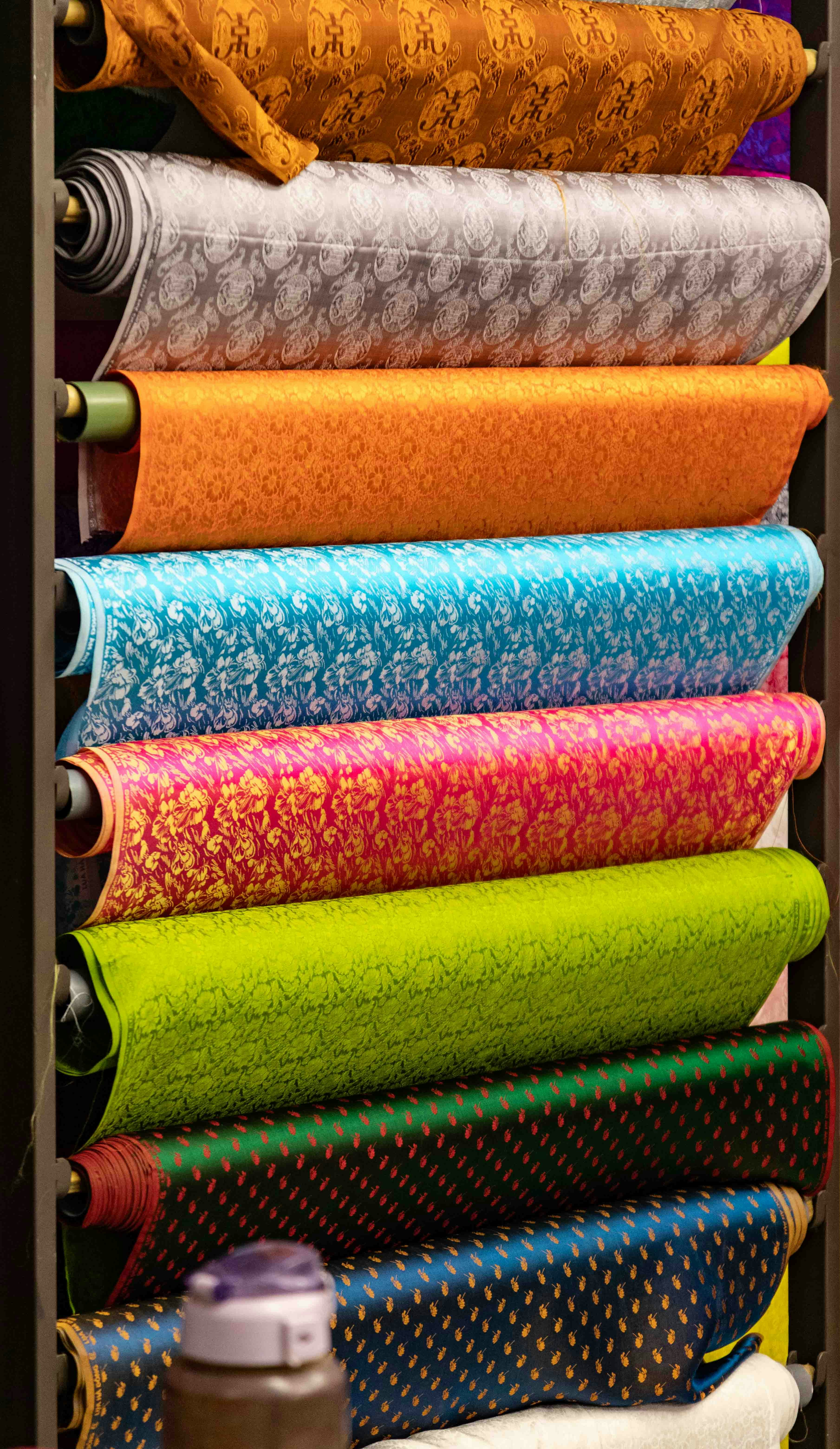 Gulungan kain bermotif warna-warni ditumpuk dengan rapi.
