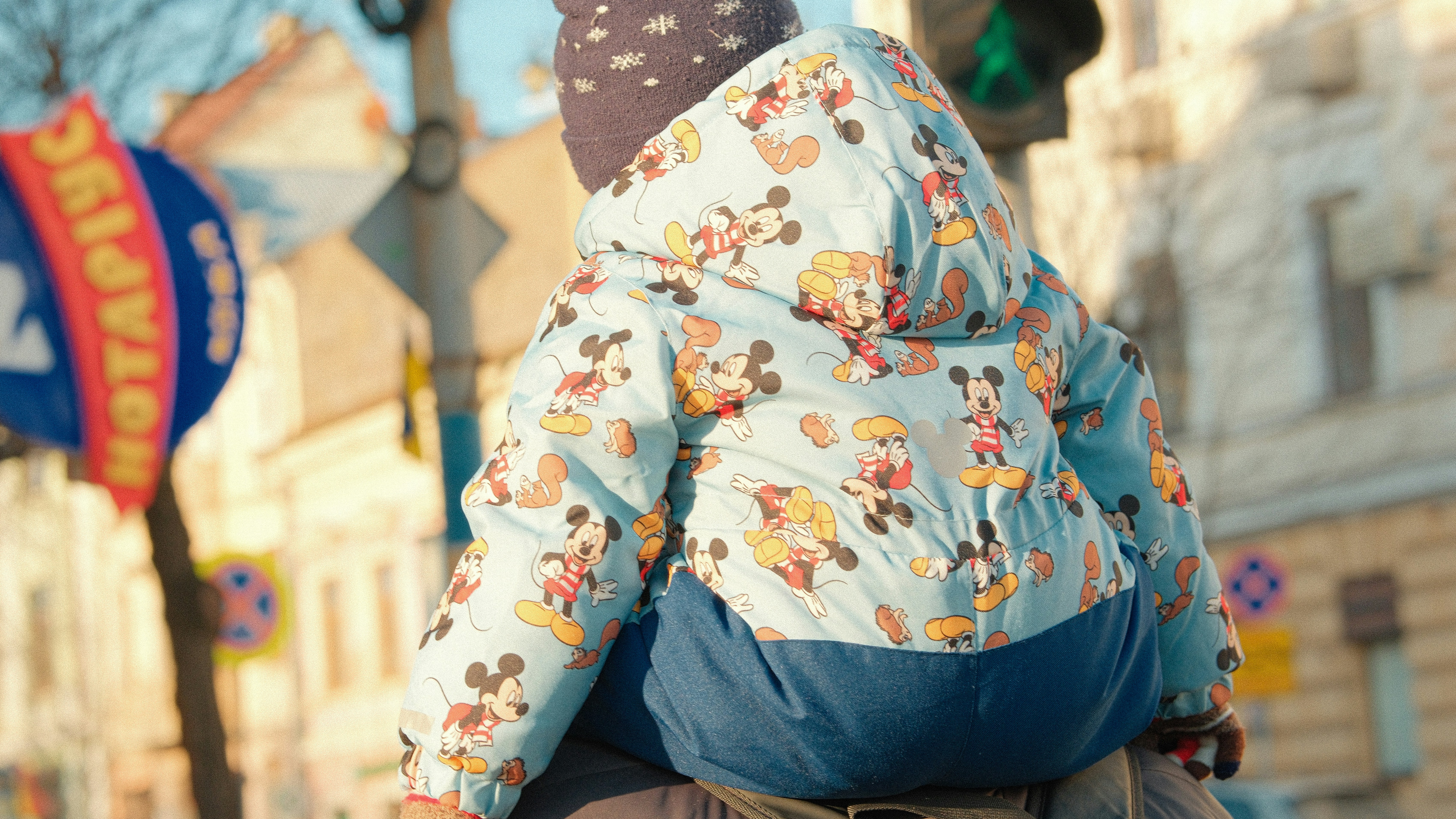 Child in mickey mouse jacket riding on shoulders
