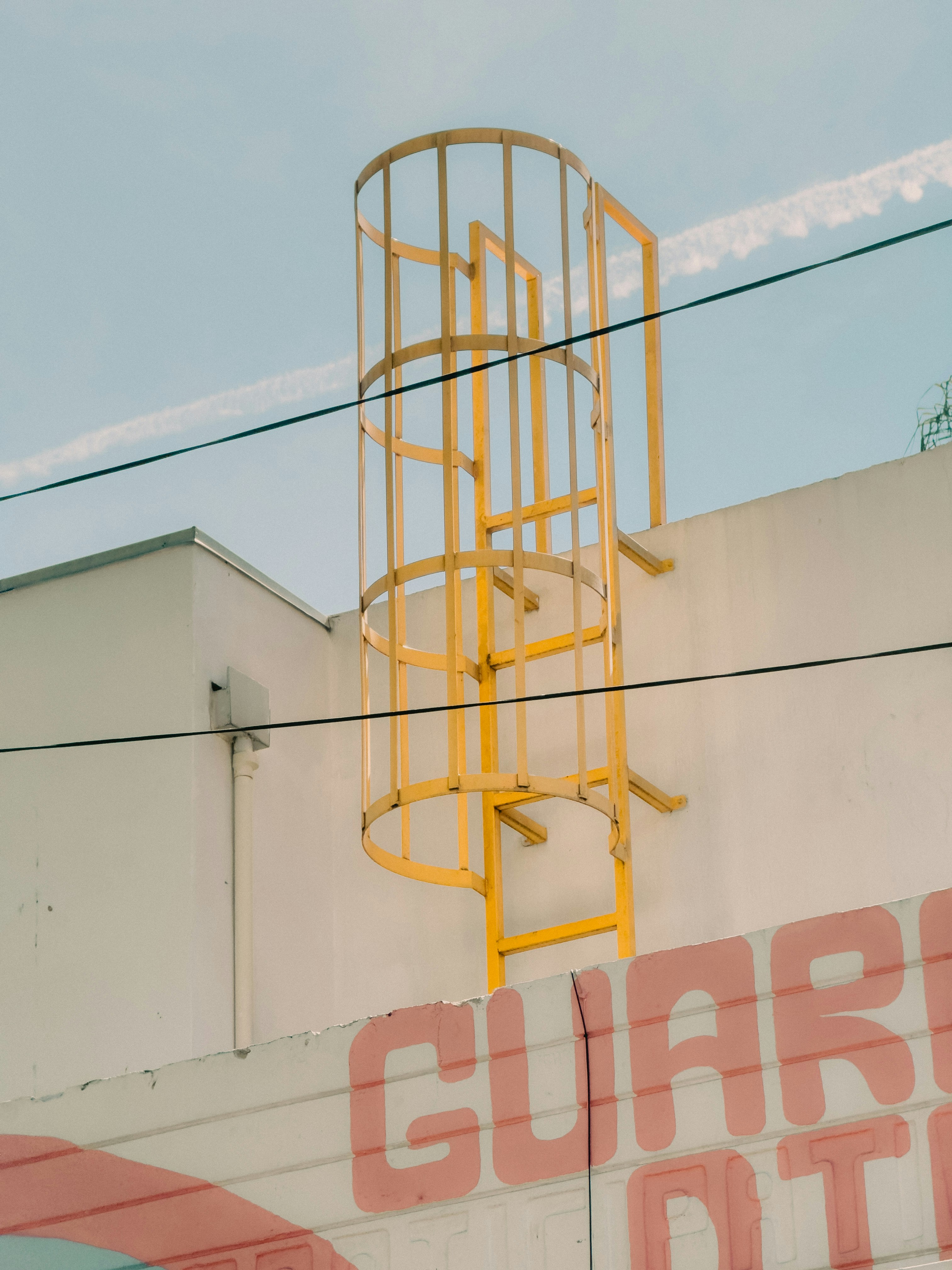 Yellow ladder on a white building with clouds