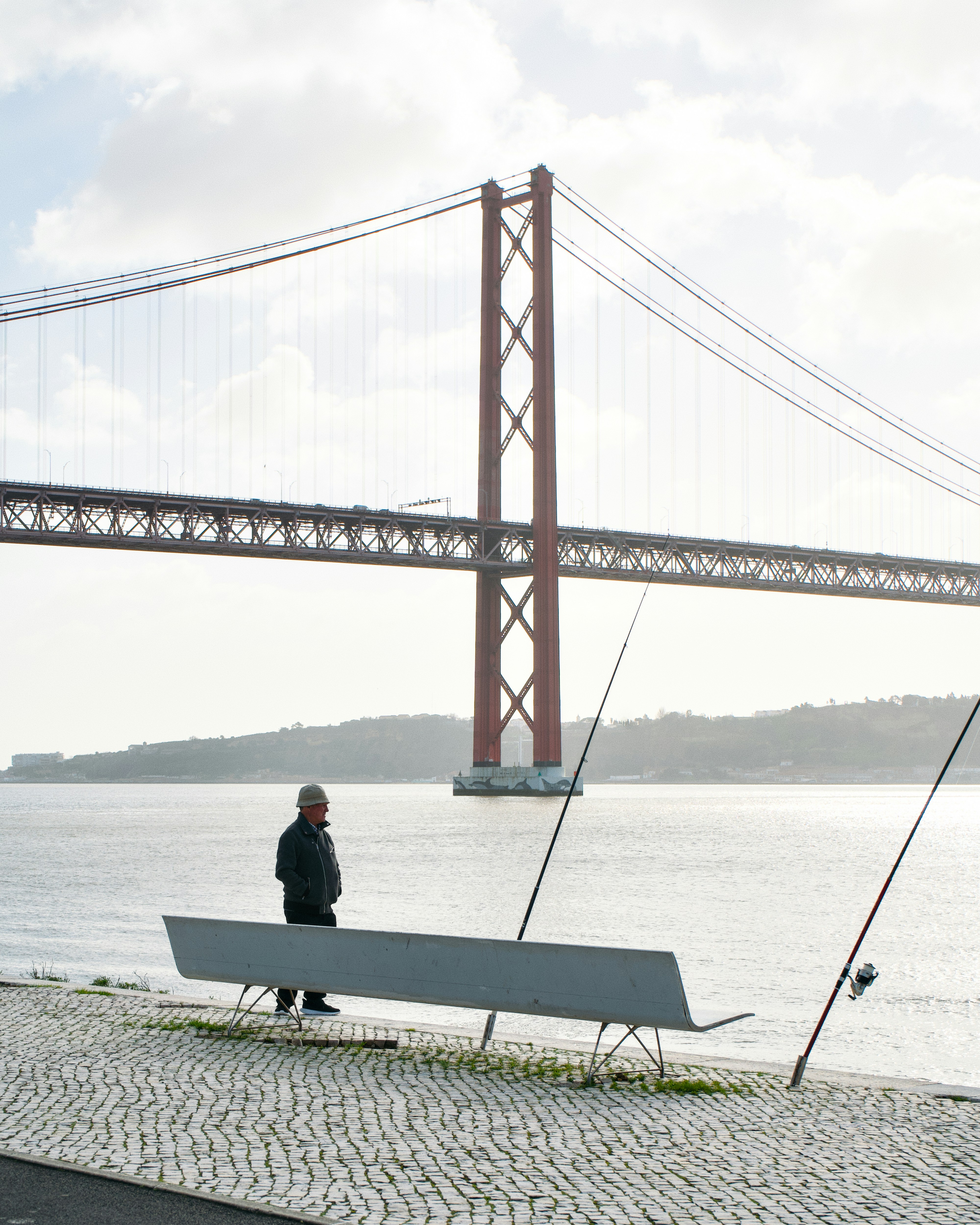 Homme sur un banc avec des cannes à pêche près du pont.