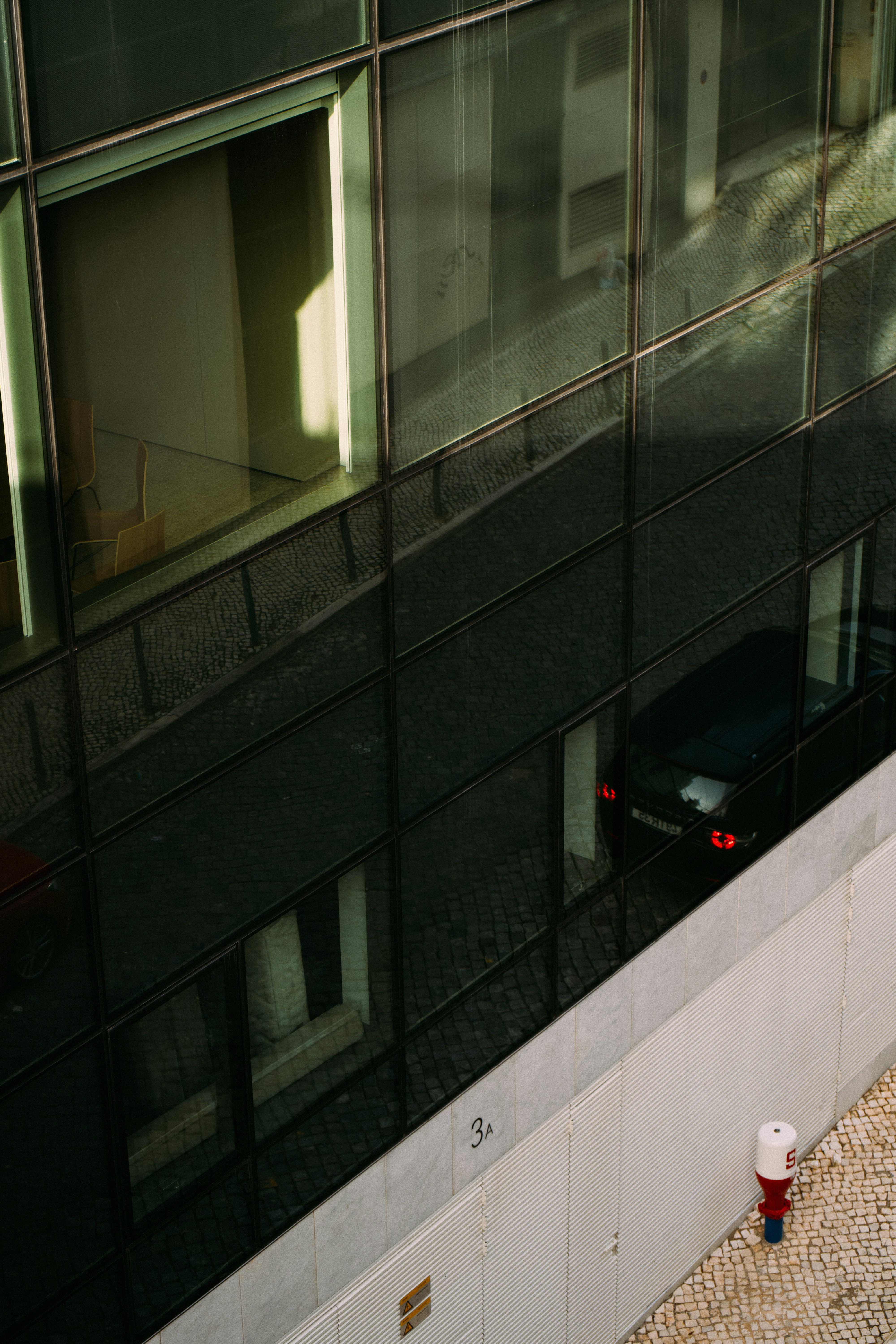 Bâtiment moderne avec une façade vitrée reflétant une voiture.