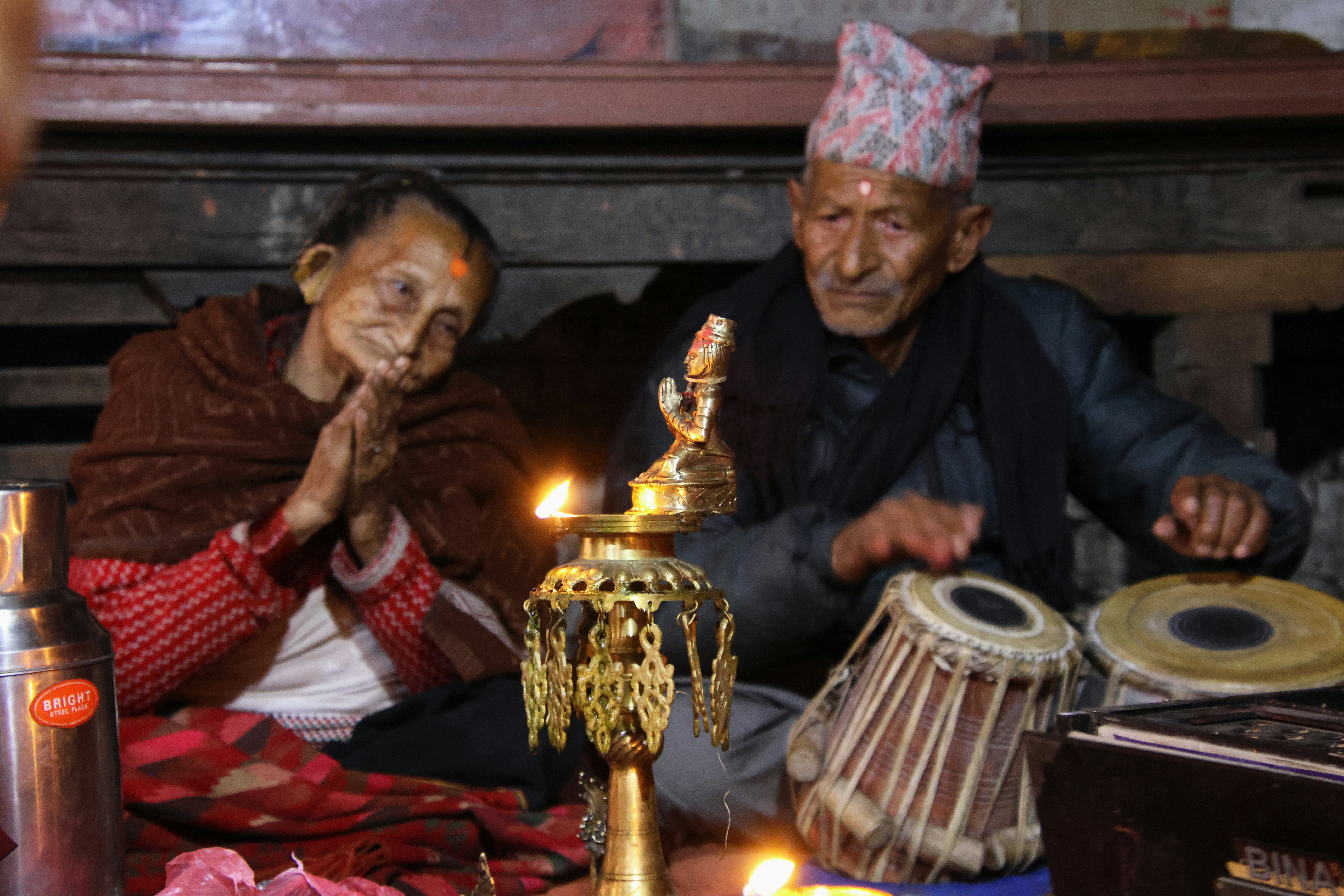 Elderly couple praying with music in a dimly lit room.