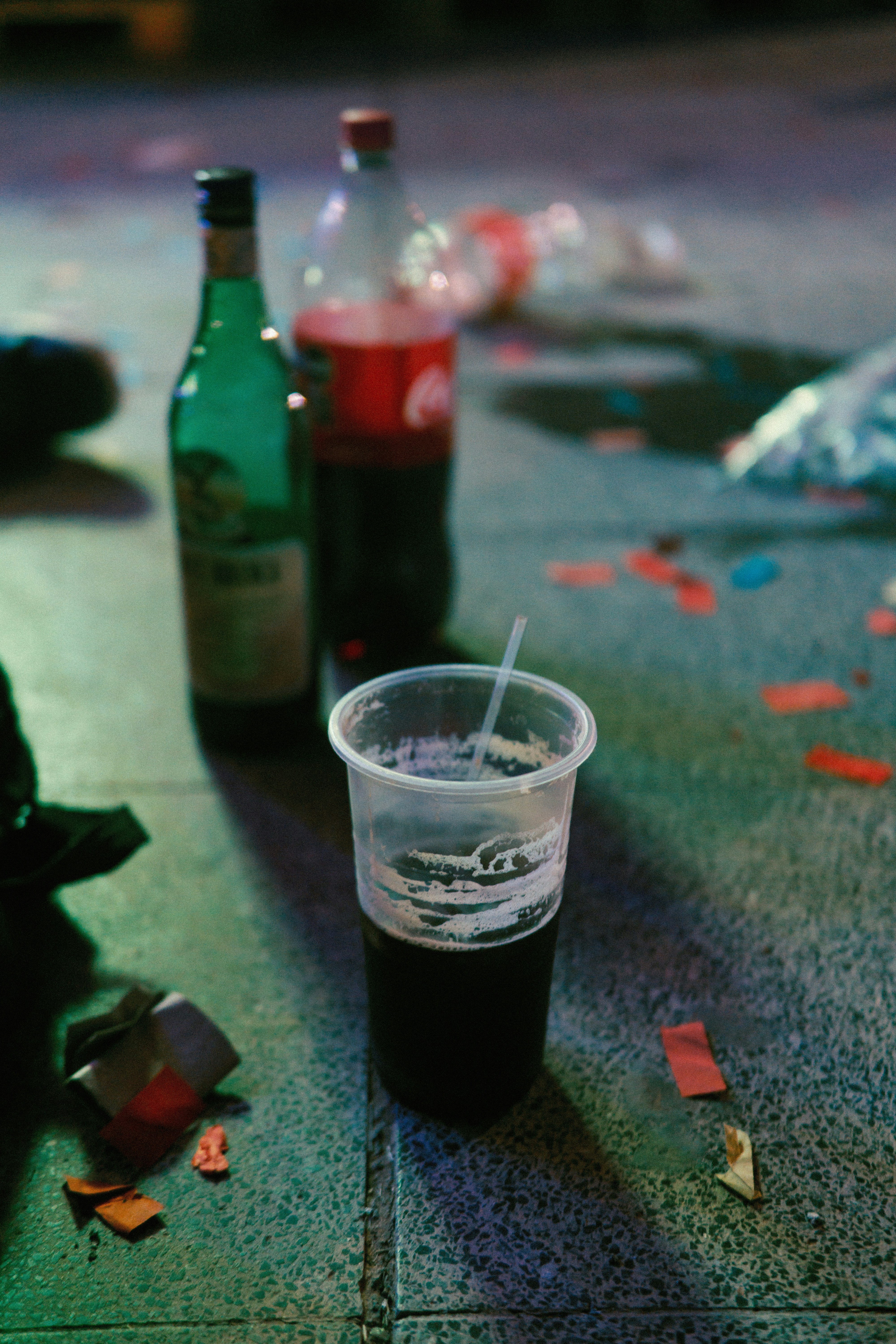 Plastic cup with straw and bottles on ground