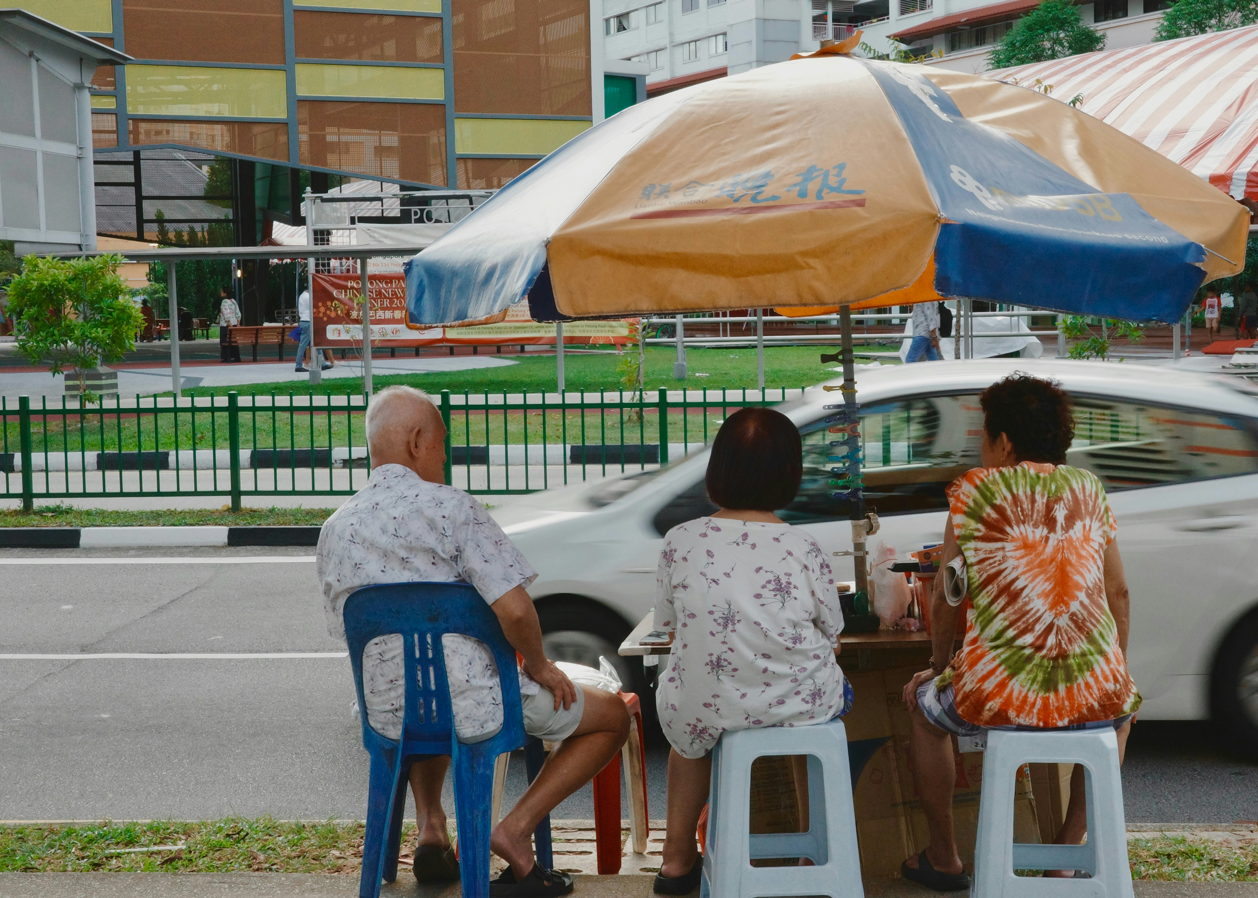 Trois personnes assises sous un parapluie au bord de la route