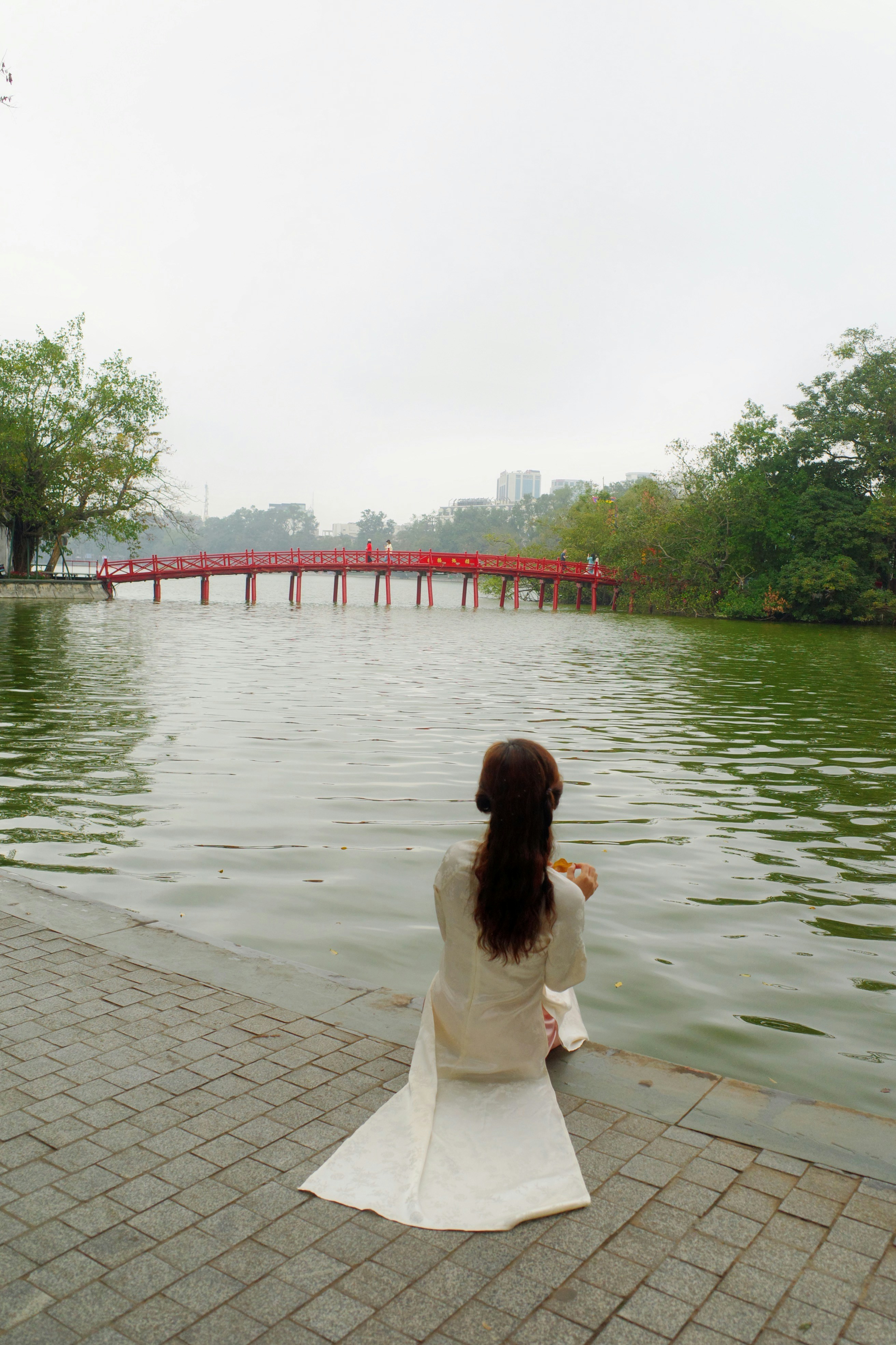Woman in white dress by lake with red bridge