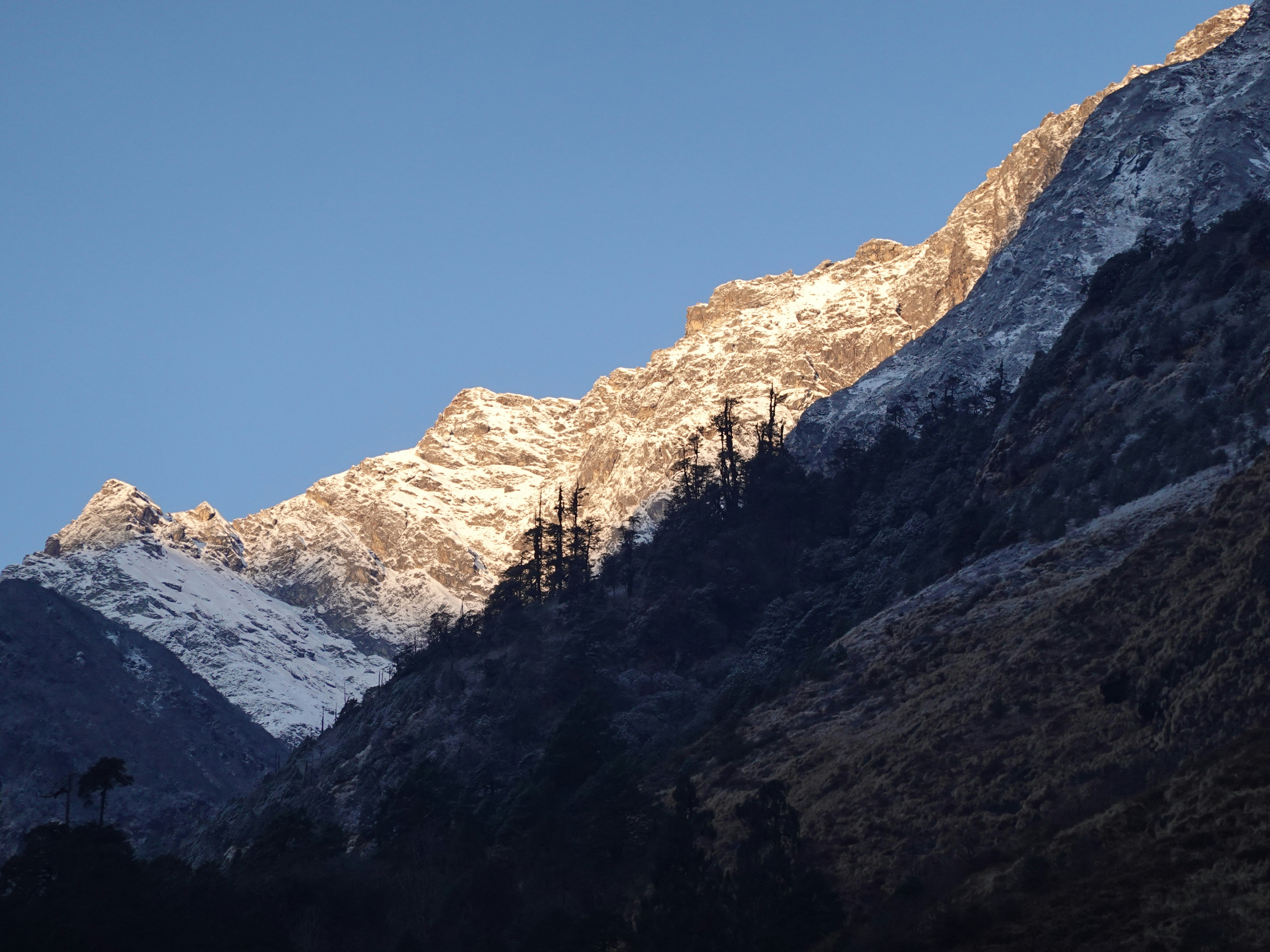 Sunlight illuminates snow-capped mountain peaks against blue sky.