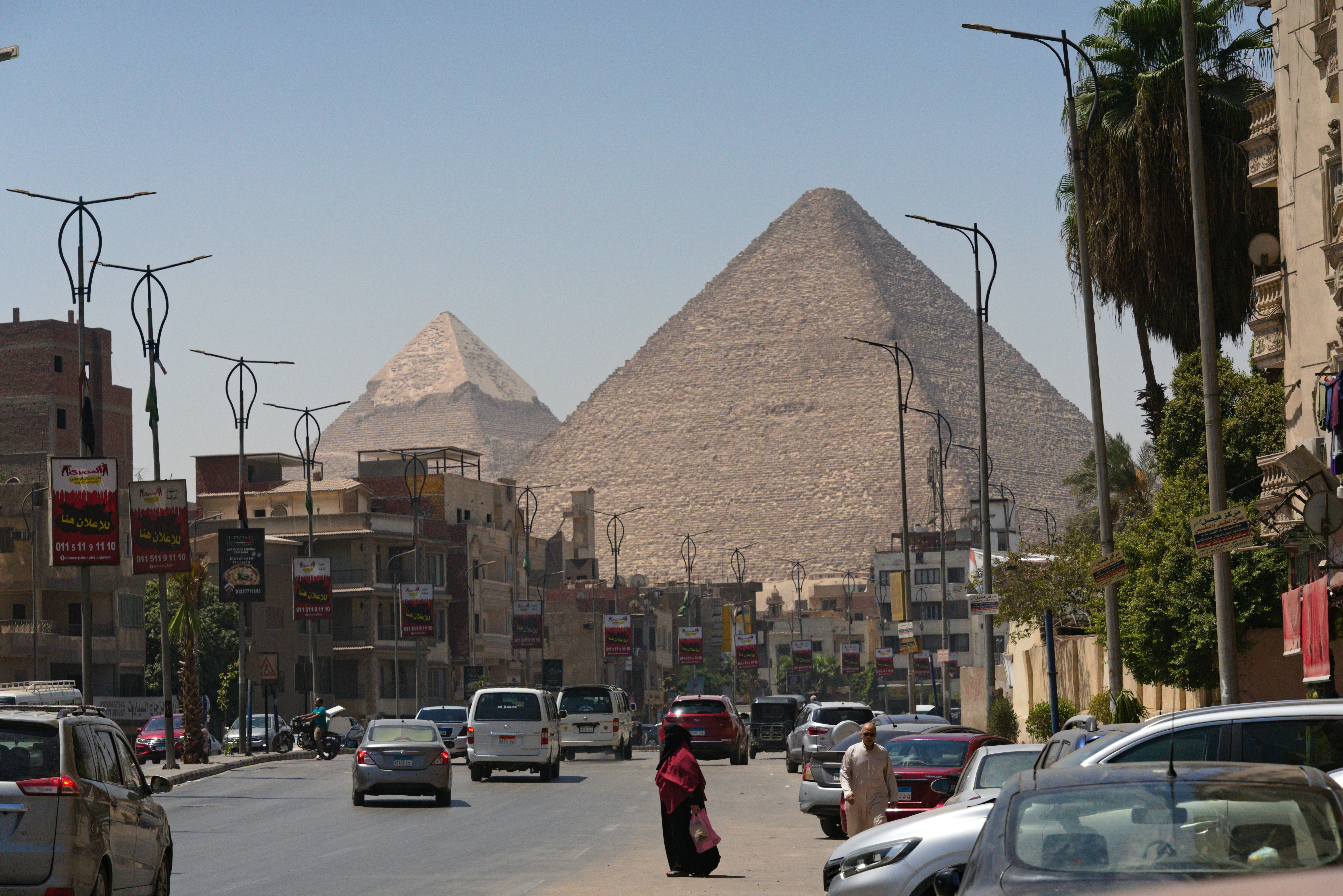 The great pyramids of giza rise behind a busy street.