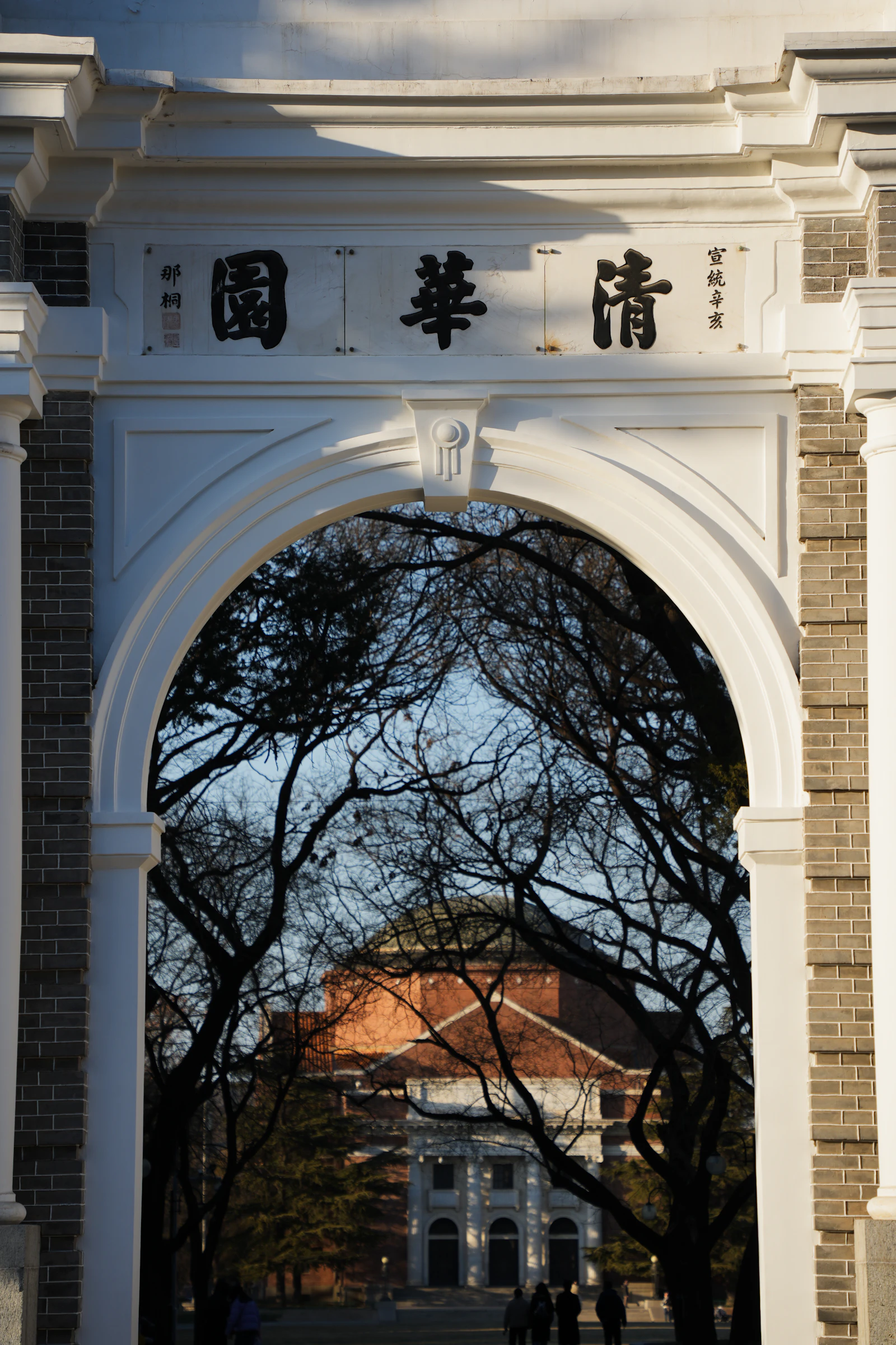A stone archway with Chinese characters, with bare winter trees behind it