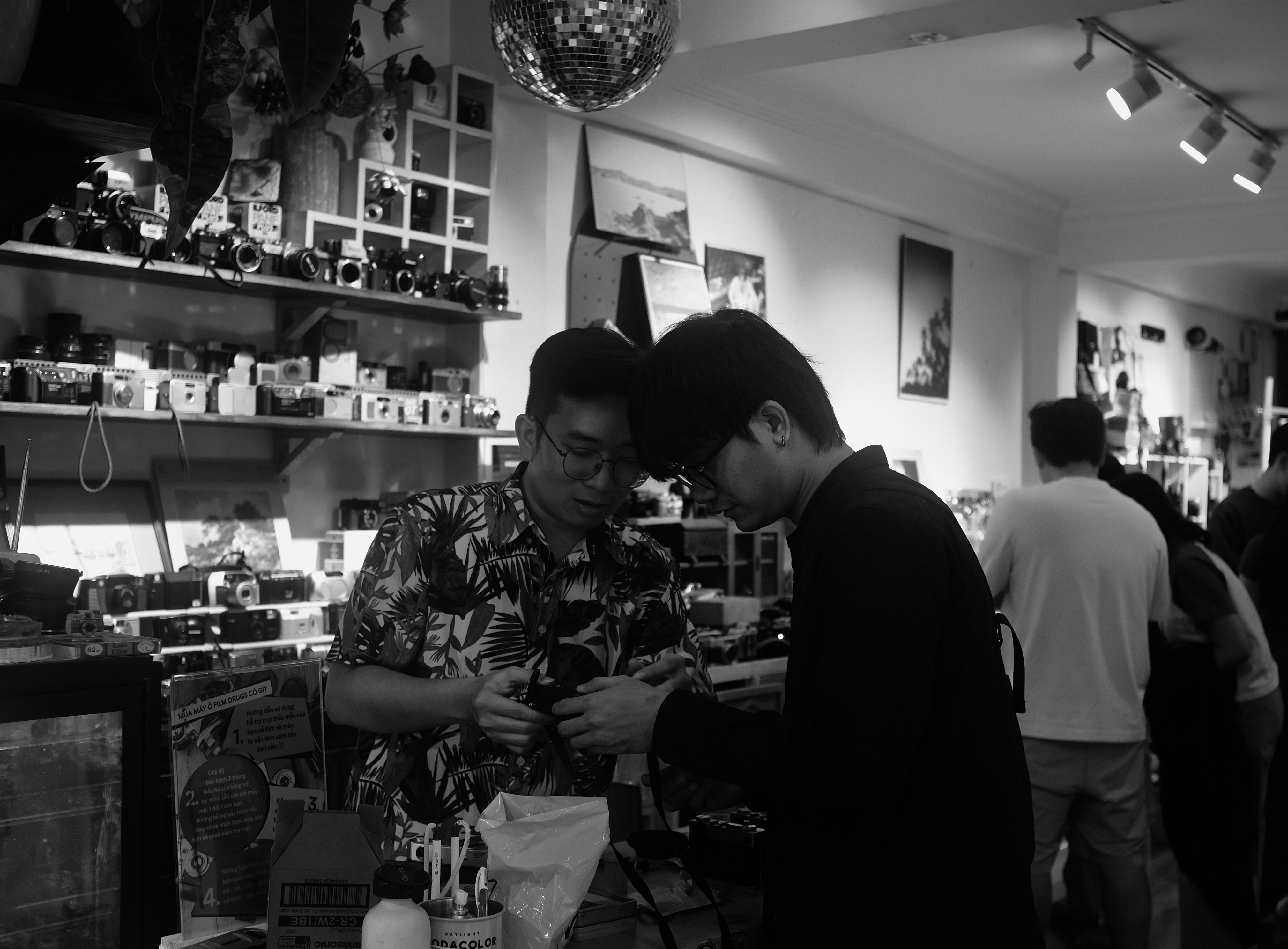 Two men examine something in a cluttered shop.